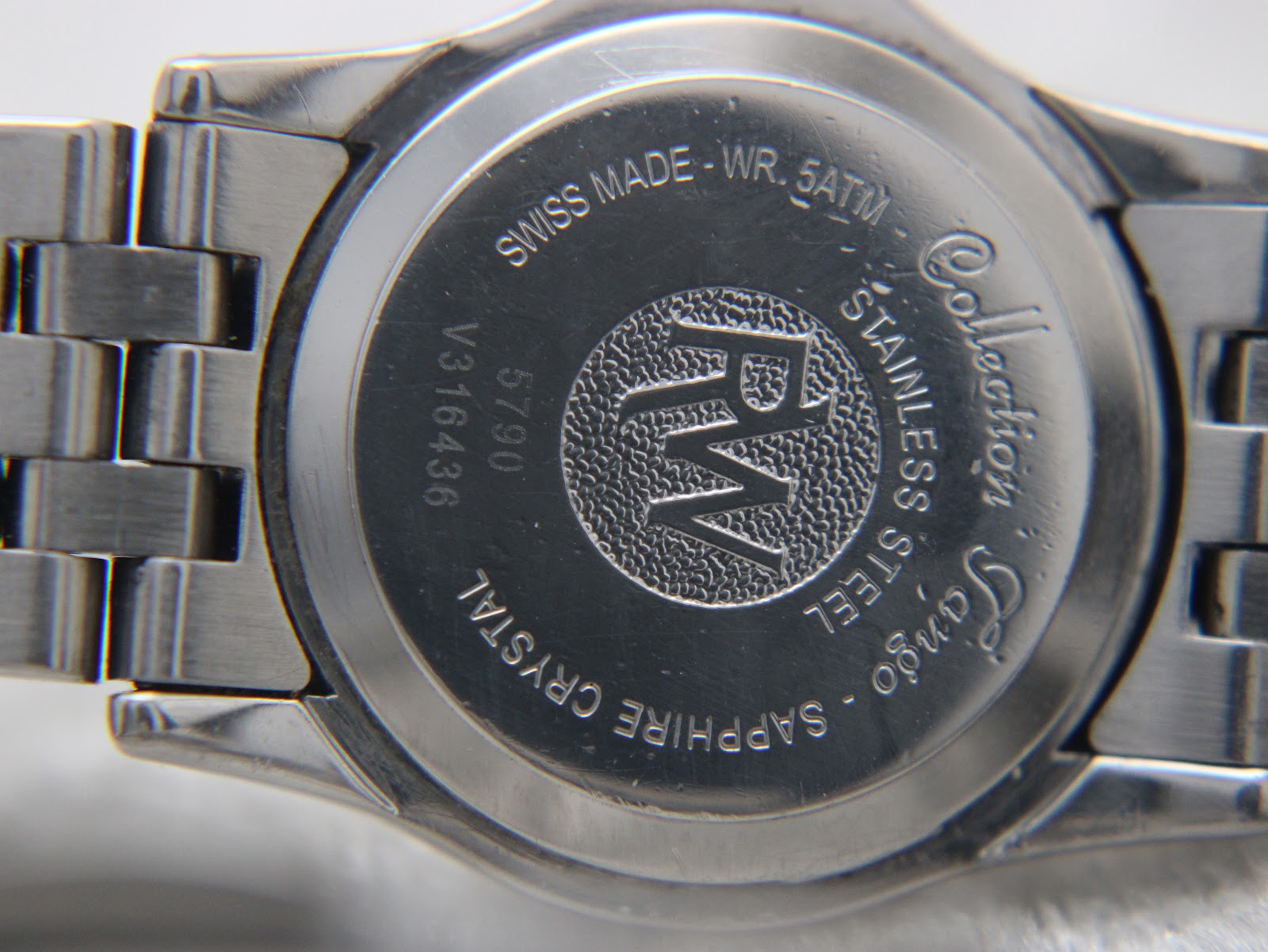 Close-up of the watch's stainless steel case back, engraved with "Swiss Made - WR. 5ATM", "Stainless Steel", "Sapphire Crystal", "Tango Collection", "RW" logo, and serial number "V316436 5790".