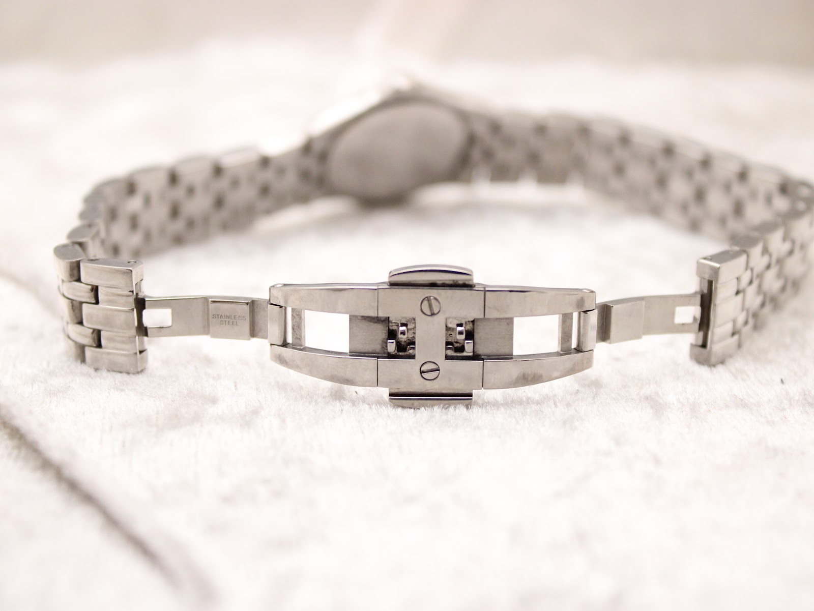 Close-up of the Raymond Weil stainless steel bracelet's double folding clasp, showing its "stainless steel" marking and internal mechanism.