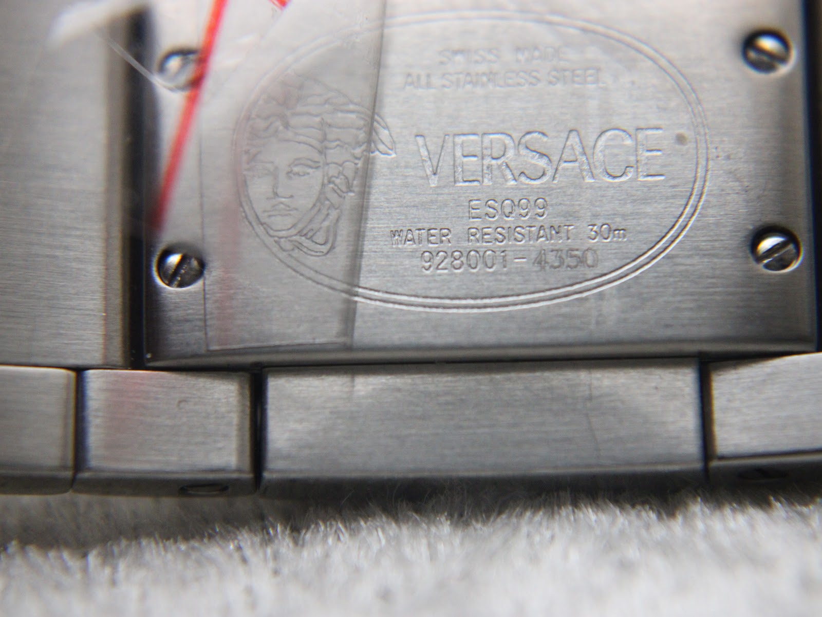 Close-up of the brushed stainless steel case back, showing Versace Medusa head logo, model, serial, and water resistance details.