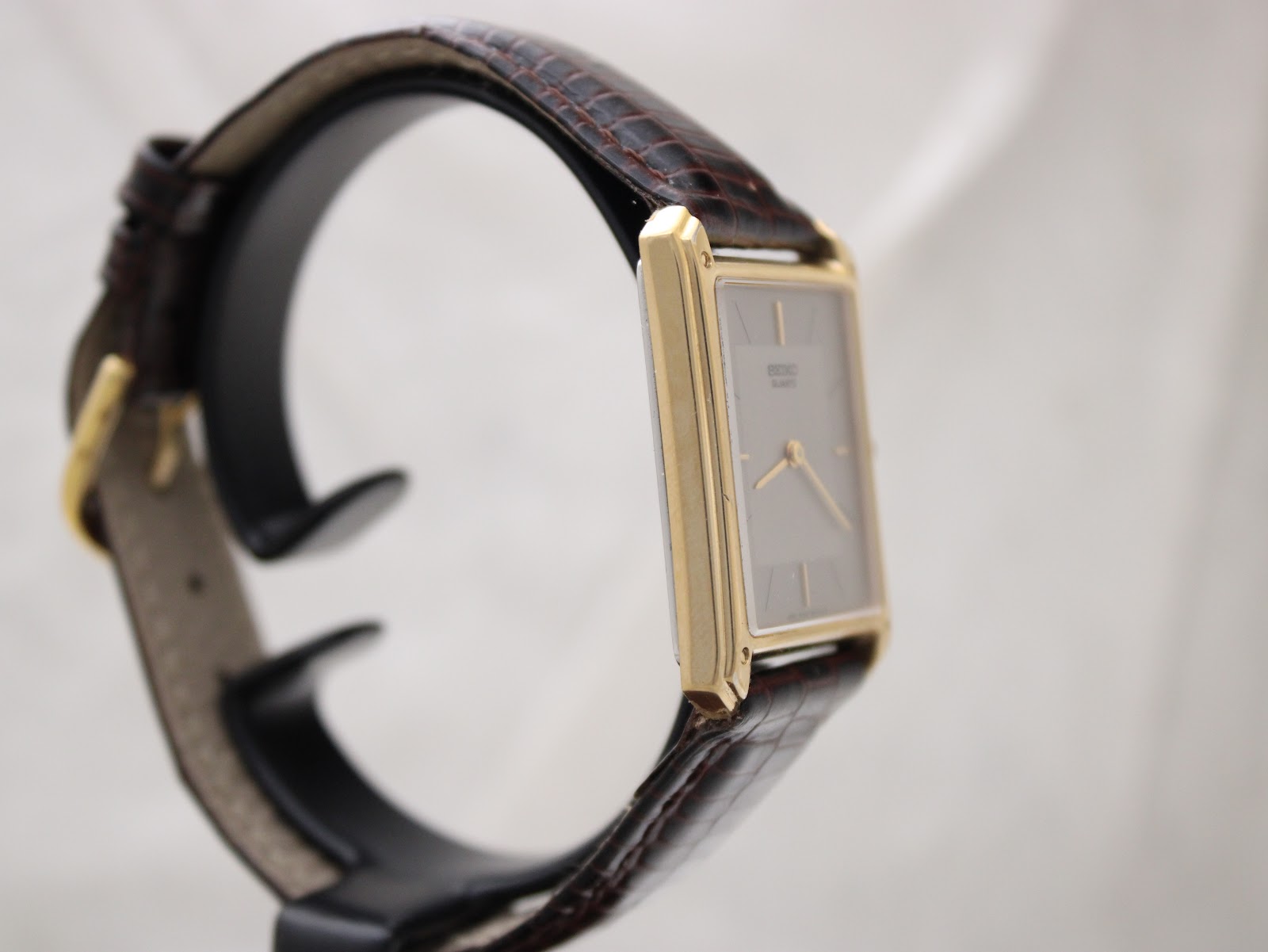 Other side profile view of the gold-tone rectangular Seiko watch on a display stand, showing the left side of the case.