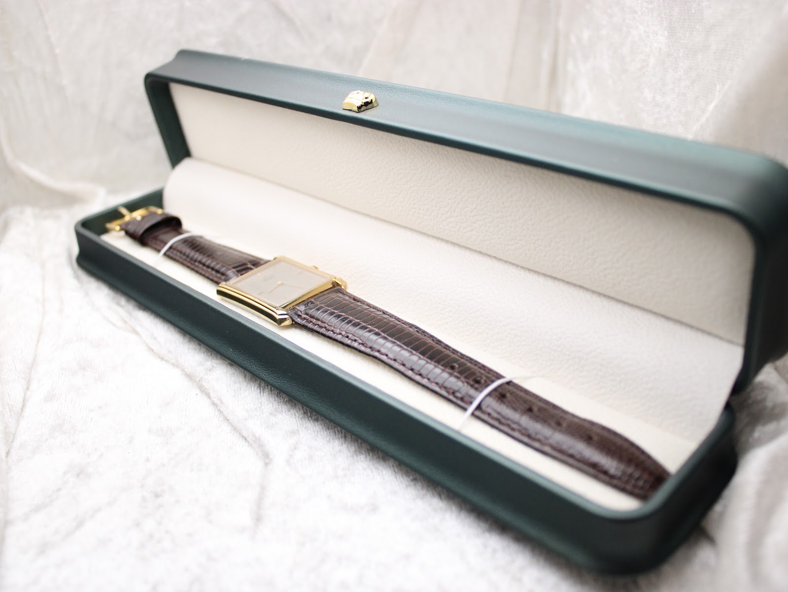 The gold-tone Seiko watch resting inside a dark green presentation box with a cream interior, shown from a side perspective.