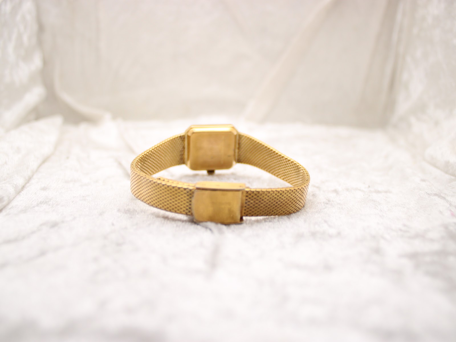 Rear view of the watch with the bracelet clasped, resting on a white textured surface.