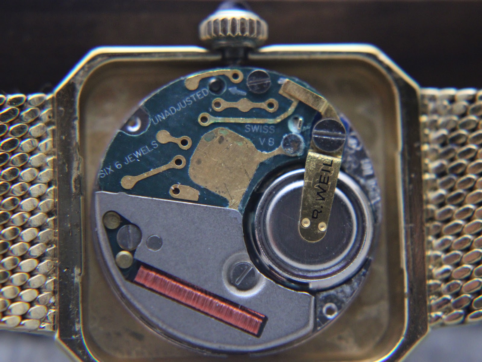 Macro shot of the watch's Swiss quartz movement, showing 'SWISS V8' and 'SIX 6 JEWELS'.