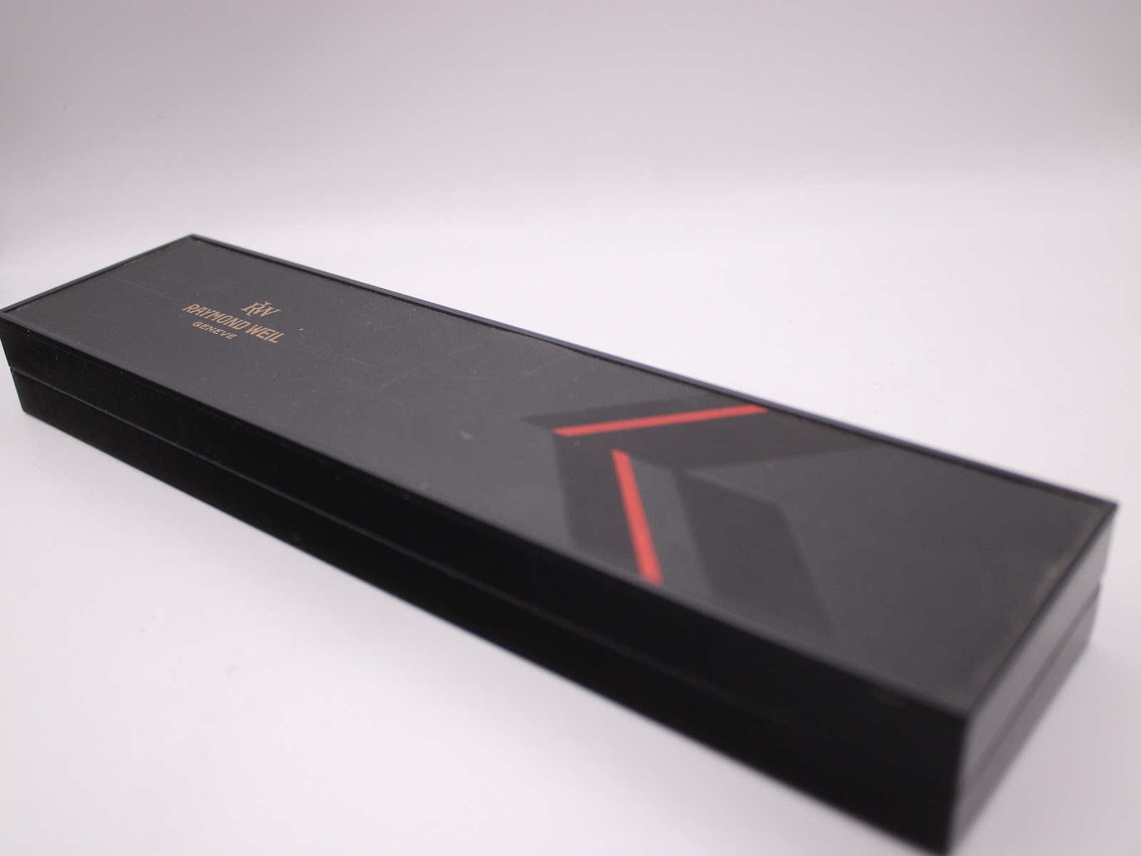 Top-down view of the closed original black Raymond Weil presentation box with branding and red stripe detail.
