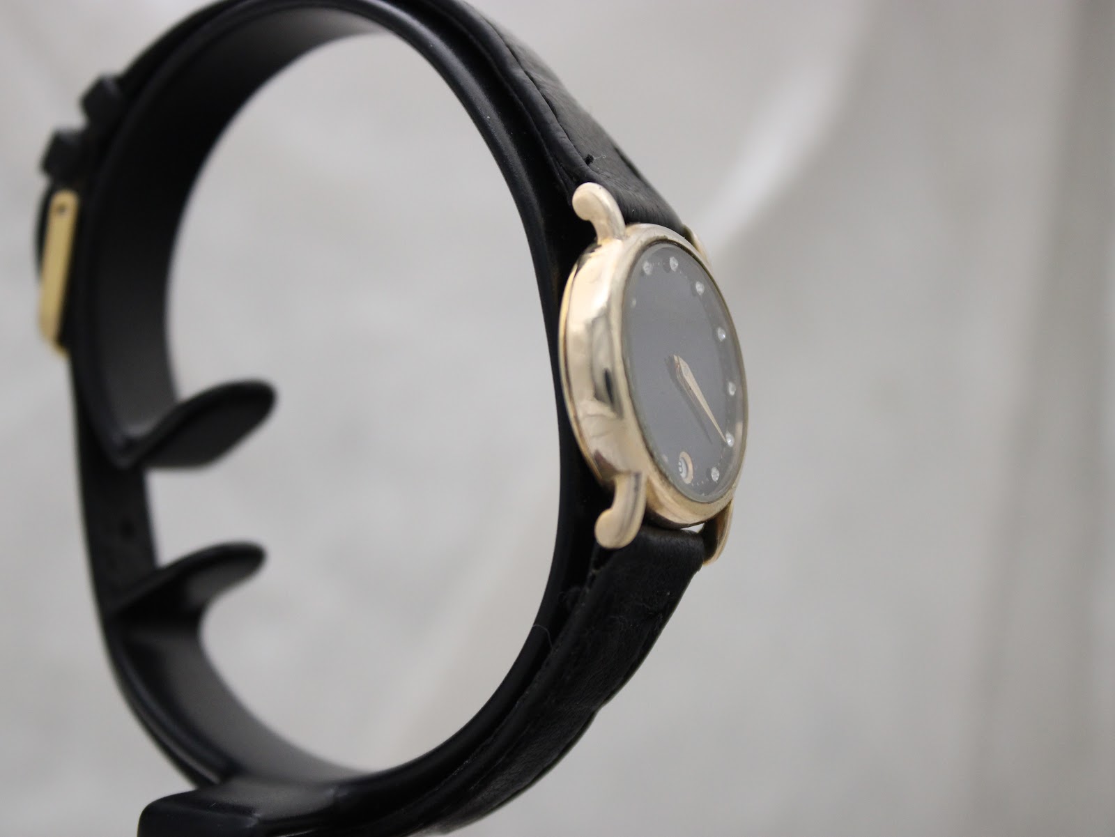 Another side view of the Raymond Weil 9923 watch on a stand, highlighting the case profile and black strap.