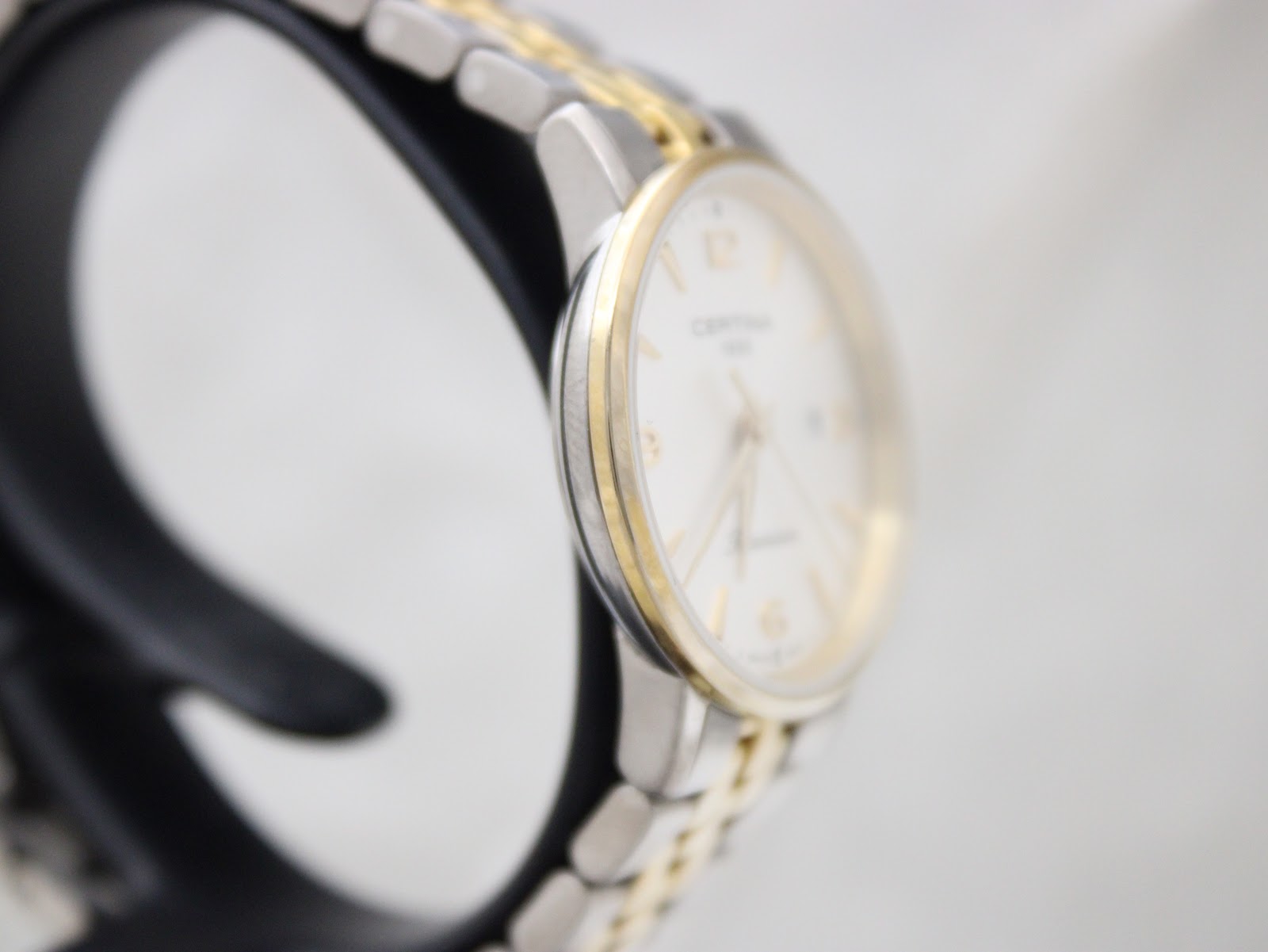 Angled side view of the Certina DS Caimano case, showing the gold-tone bezel and titanium mid-case.