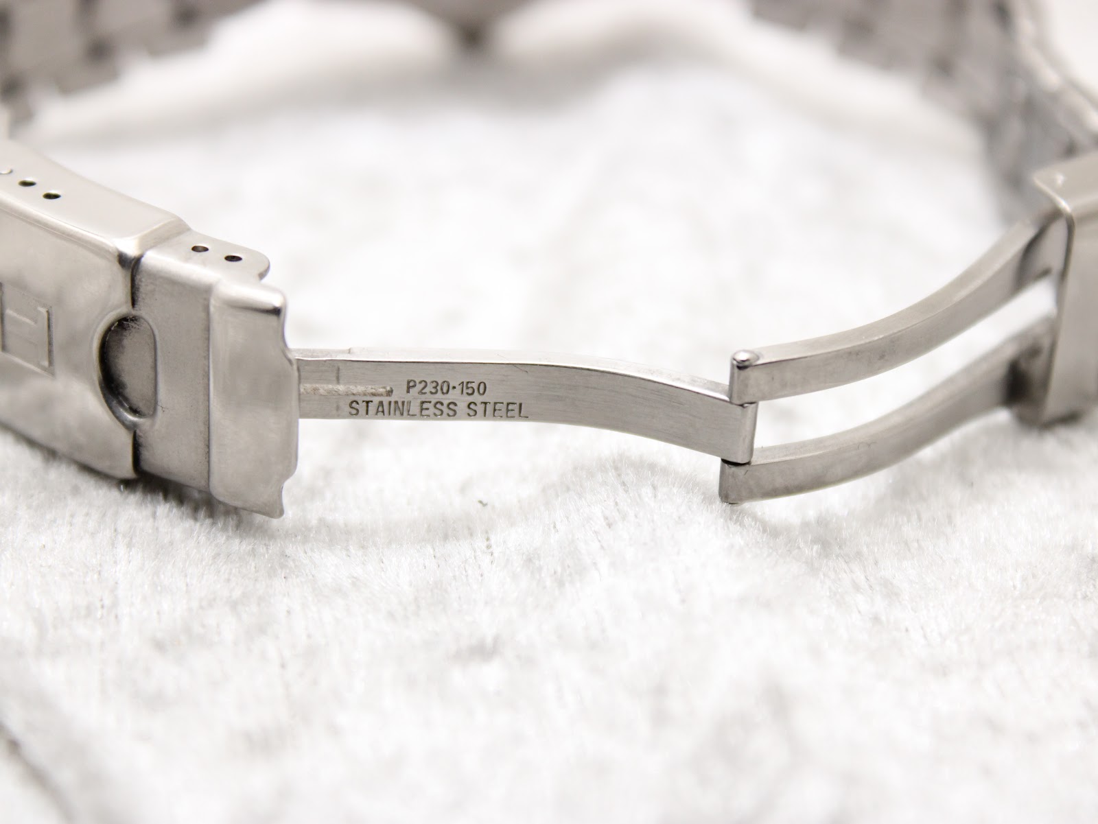 Close-up of the inside of the stainless steel bracelet's signed fold-over clasp, showing "P230-150" and "Stainless Steel" engravings.