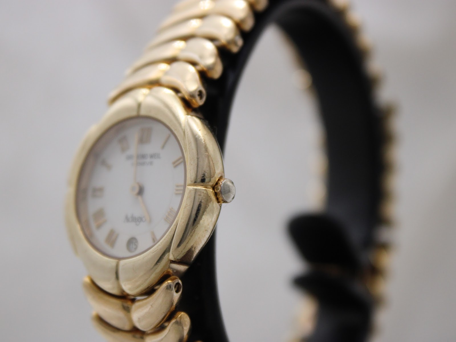 Angled side view of the Raymond Weil Adagio watch on a black stand, showing the fluted crown and curved gold-plated case.