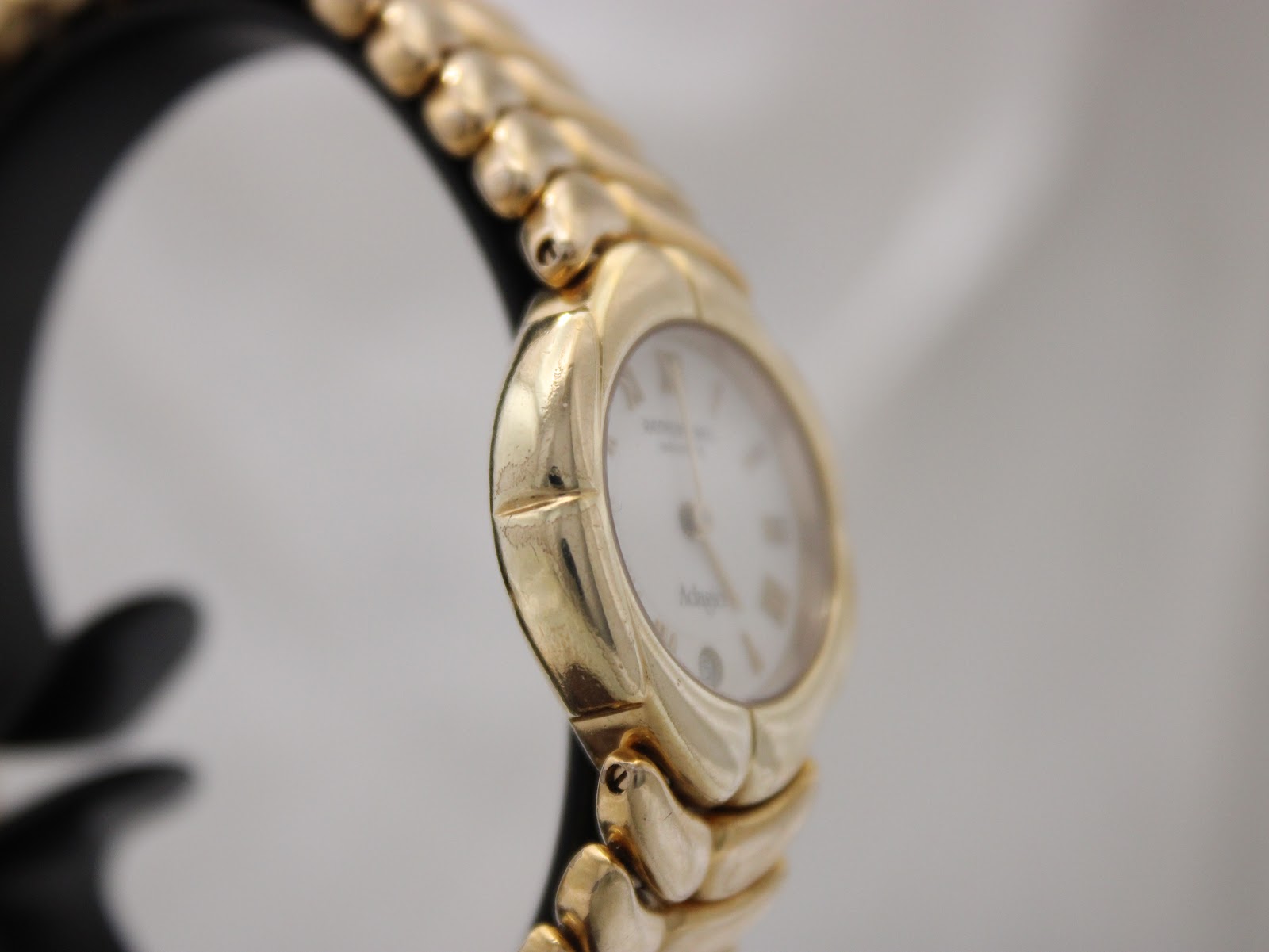 Another angled side view of the gold-electroplated Raymond Weil Adagio watch on a black stand, highlighting the integrated bracelet links.
