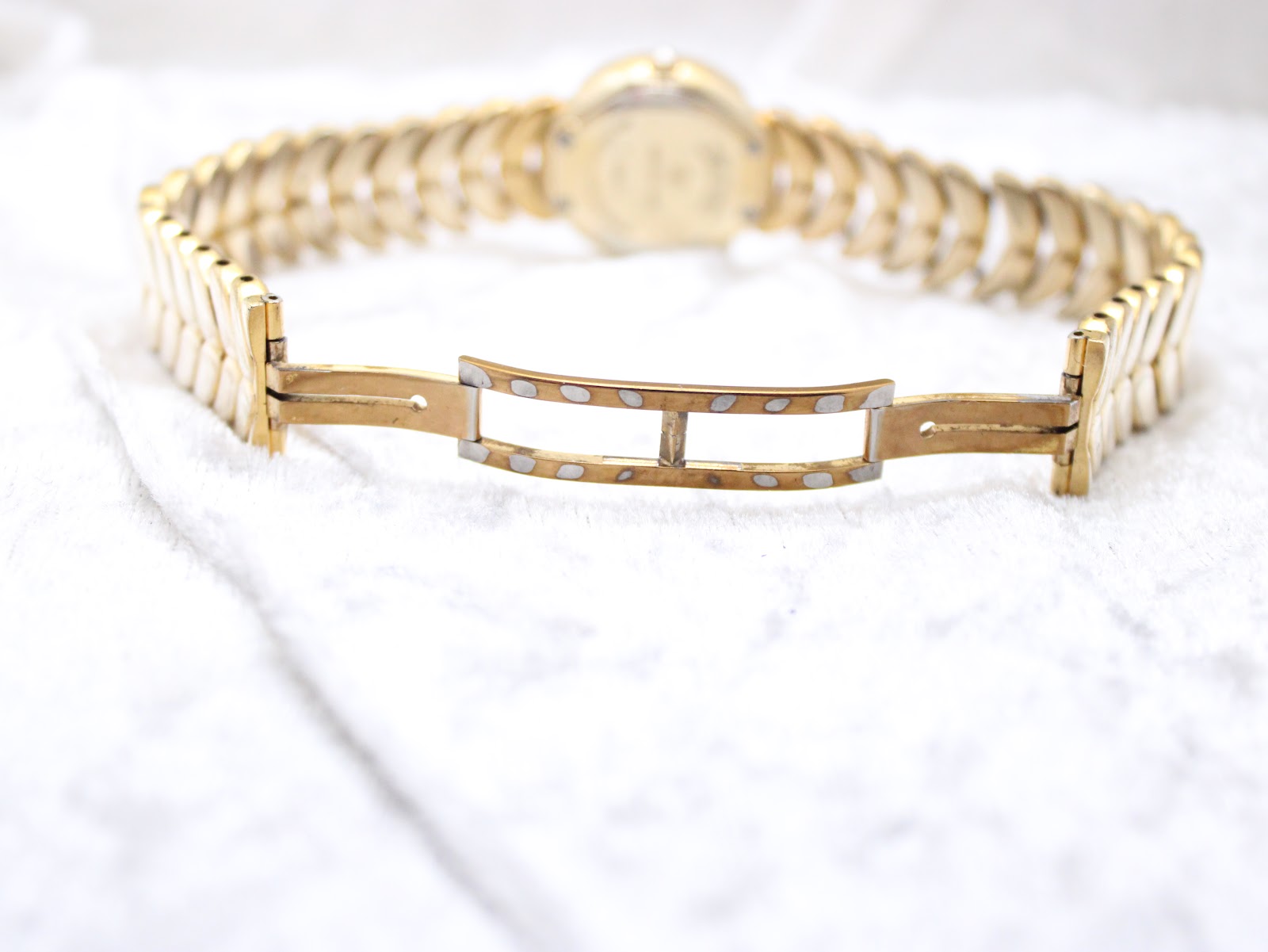 View of the hidden clasp on the integrated gold-electroplated bracelet, open and lying on a white textured surface.