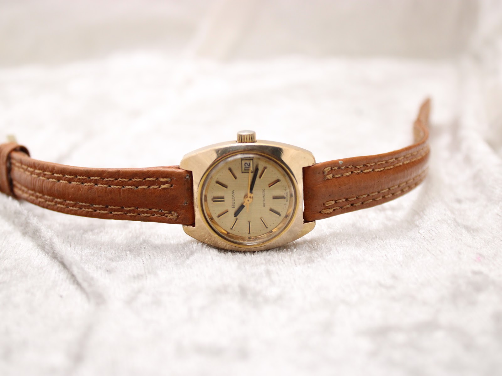 Full view of the Bulova watch with its brown leather strap laid flat on a white textured surface.