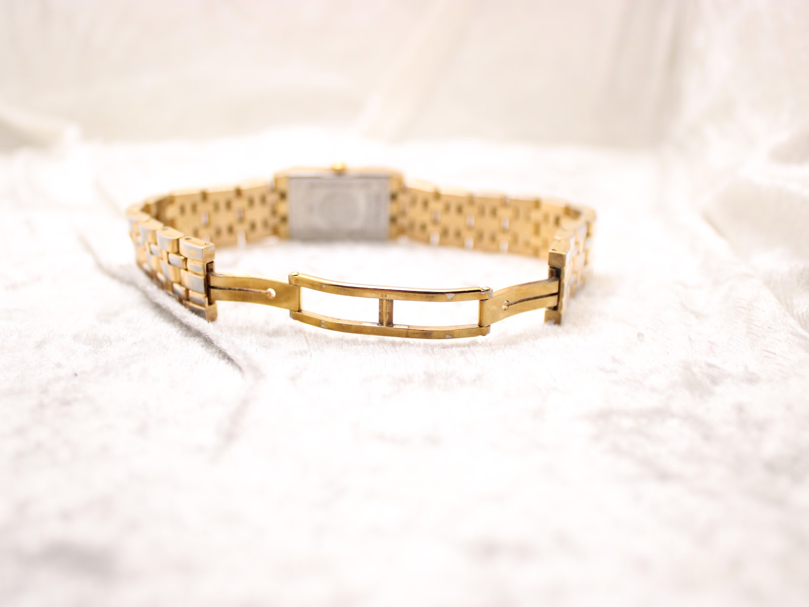 View of the gold-tone double-fold clasp and bracelet opened flat on a white textured surface.