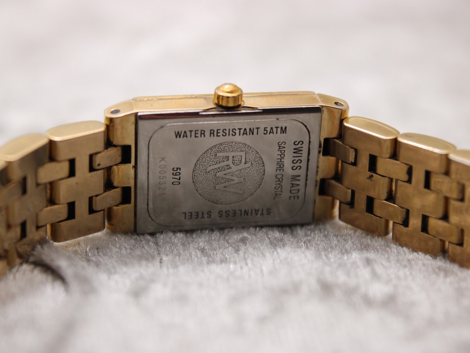 Close-up of the watch case back showing "Water Resistant 5ATM", "Swiss Made", "Sapphire Crystal", "Stainless Steel", "5970", and serial number "K005321".