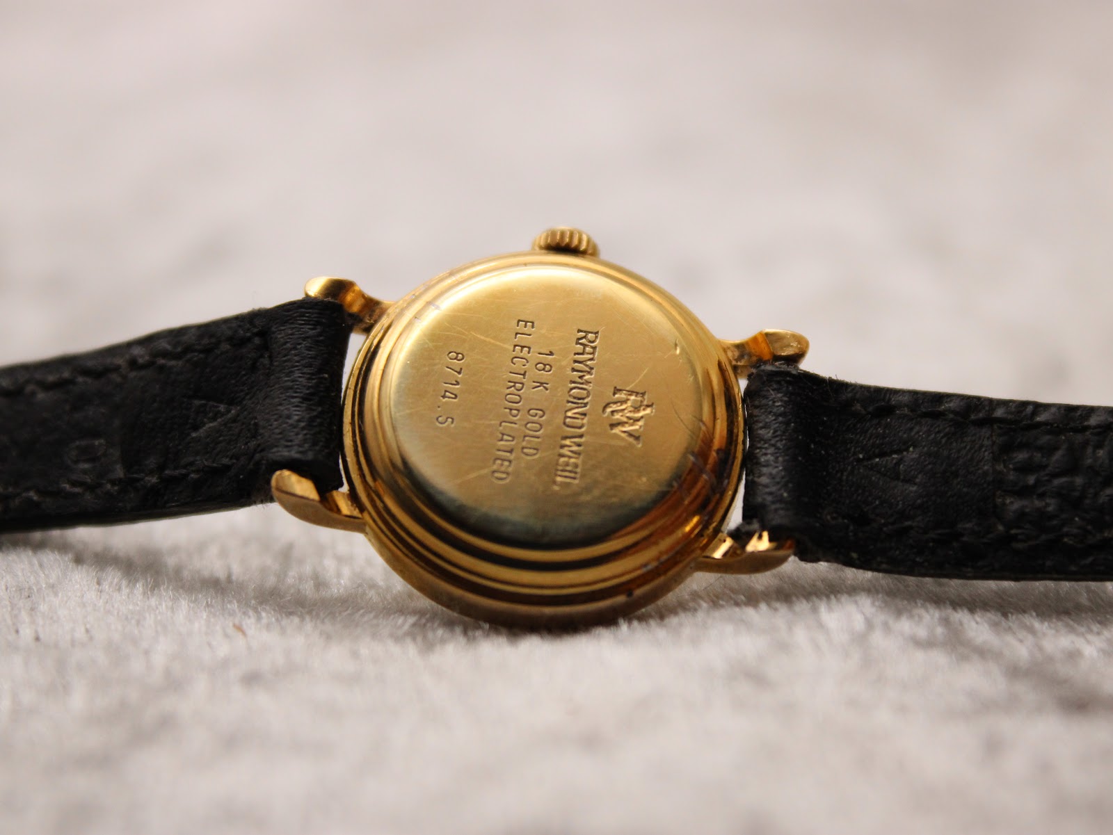 Close-up of the watch case back, showing "RAYMOND WEIL", "18K GOLD ELECTROPLATED", and model "8714-S" engravings.