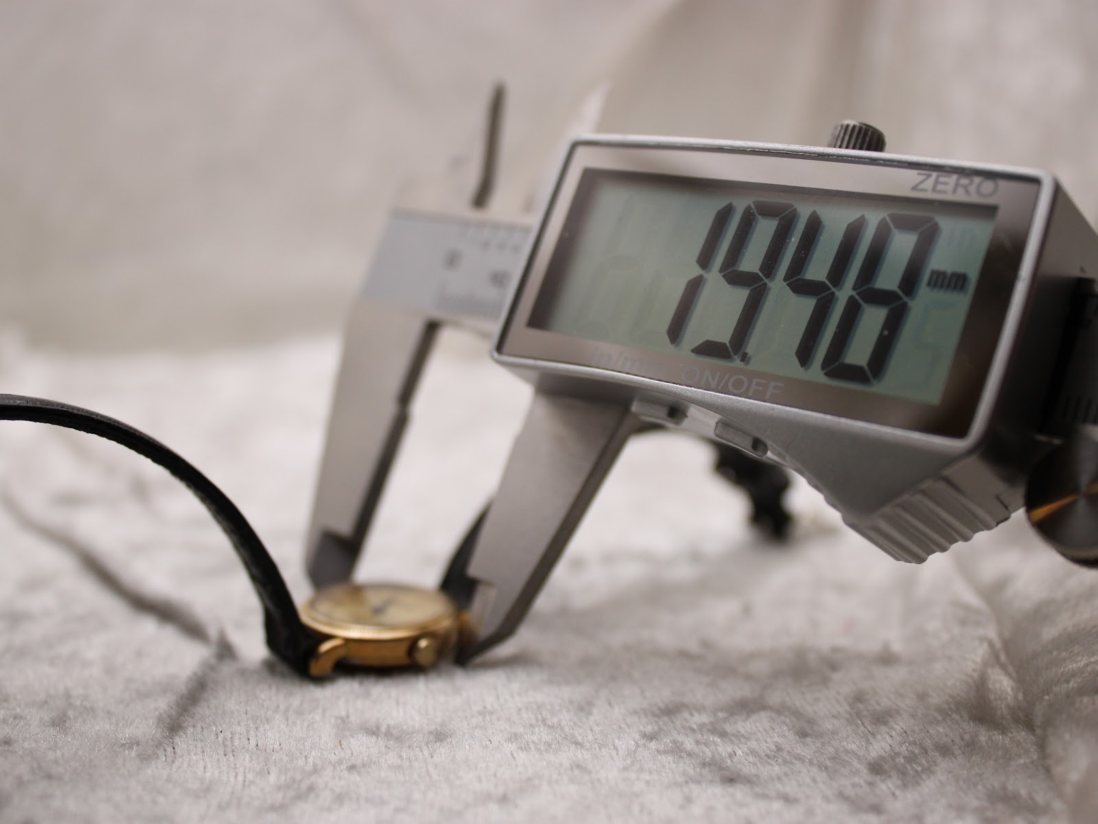 Digital caliper measuring the watch case, displaying a diameter of 19.40 mm, with the watch resting on a light-coloured surface.