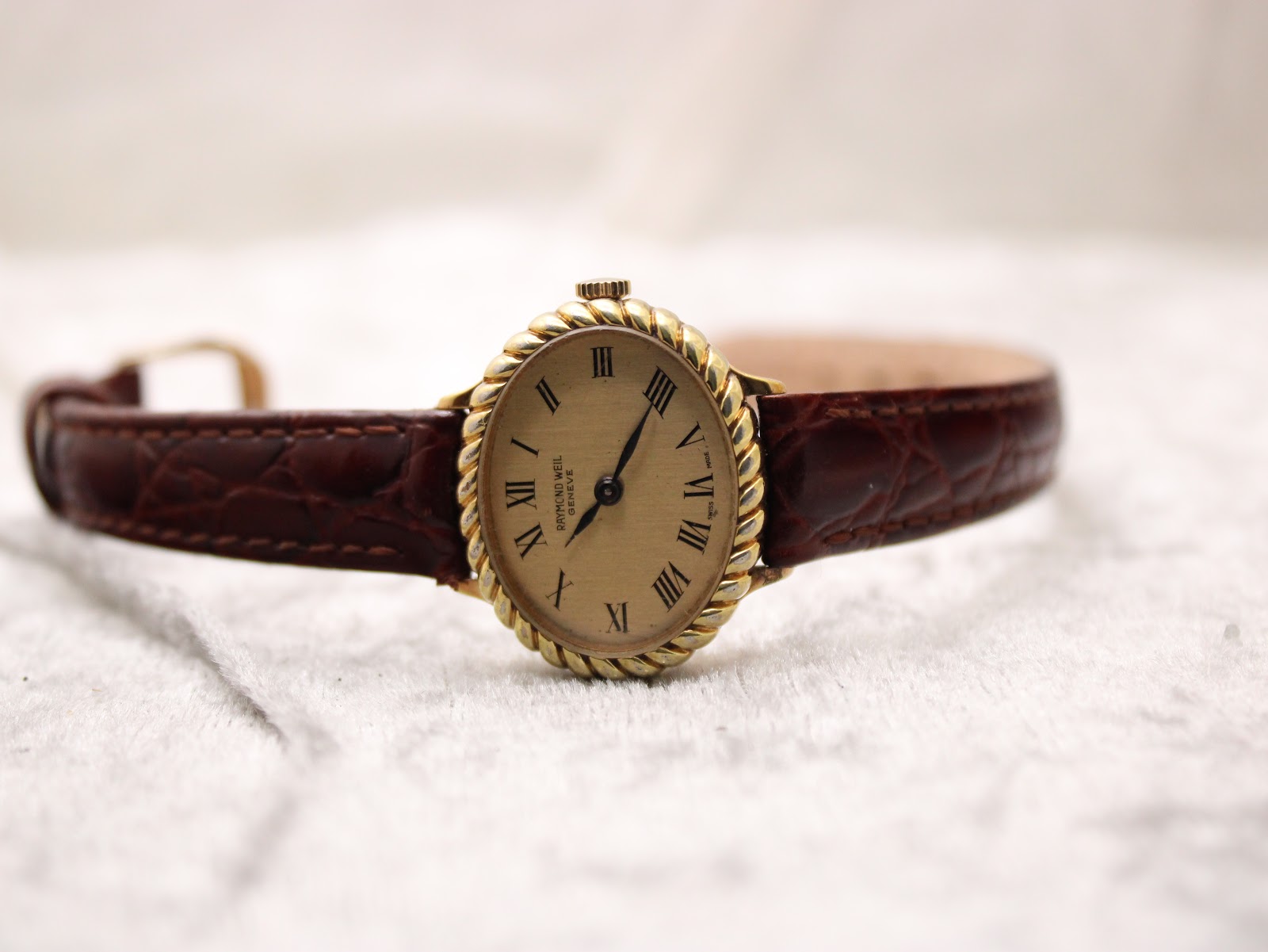 Overhead front view of the Raymond Weil 683 watch laid flat, displaying the extended brown crocodile-patterned leather strap and the oval Roman dial.