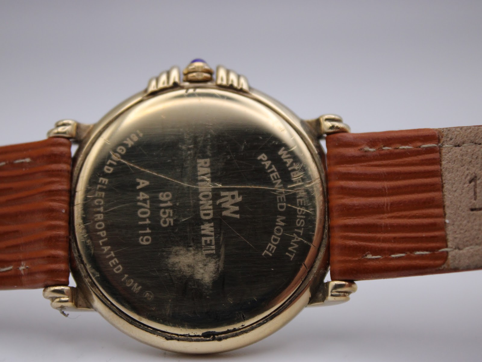 Close-up of the gold-plated case back showing Raymond Weil, 9155, A470119, 18k gold electroplated, and water resistant engravings with wear.
