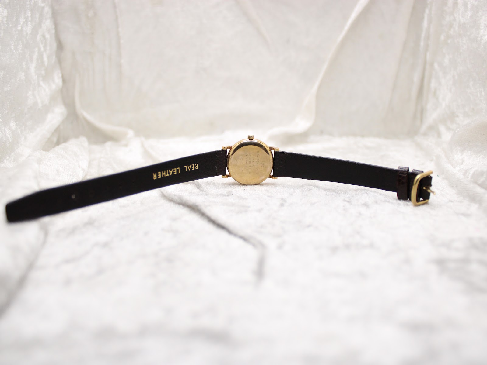 Back view of the Raymond Weil watch with the brown leather strap extended, showing the case back and 'REAL LEATHER' marked on the strap interior.