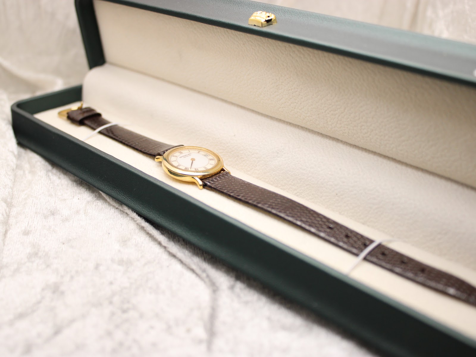 The Raymond Weil watch neatly placed inside a dark green presentation box with an off-white interior.