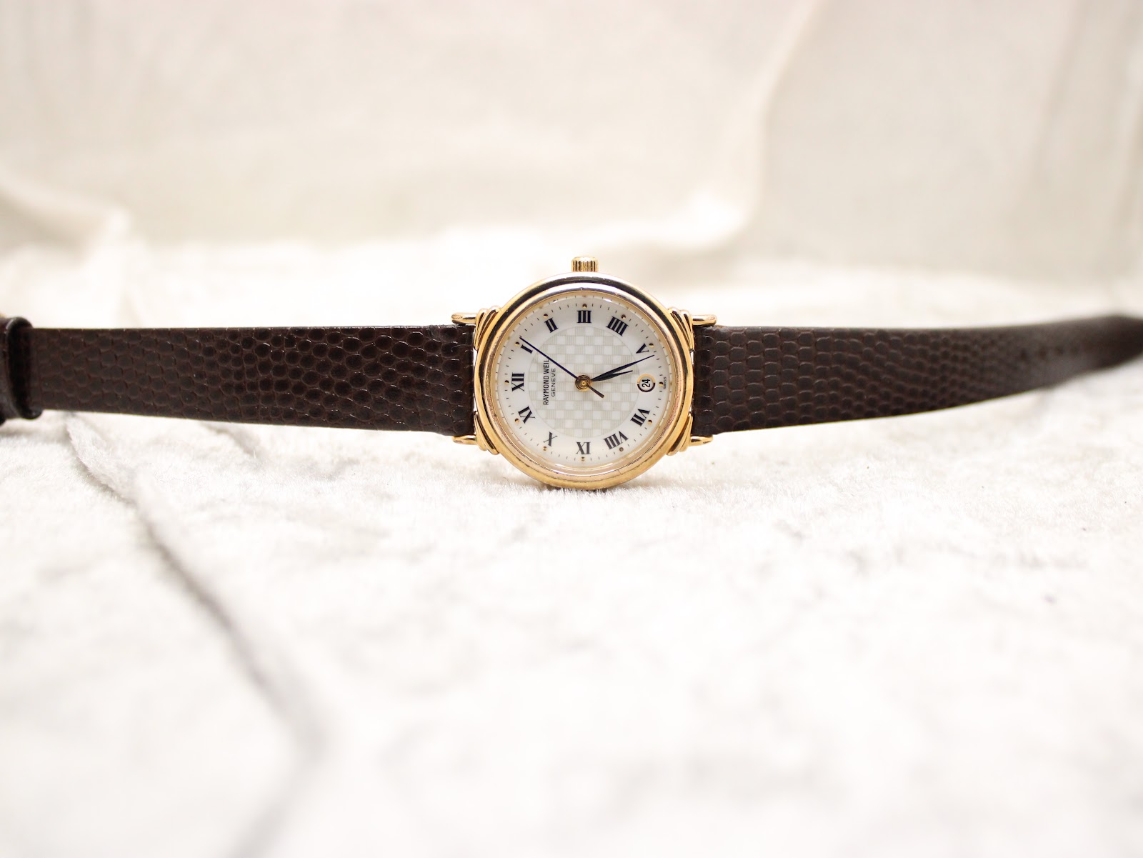 Top-down view of the Raymond Weil 5331 watch with its brown leather strap laid flat on a white textured surface.