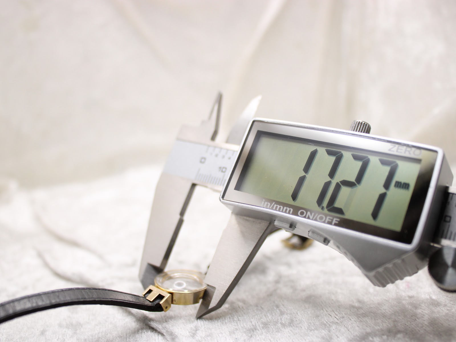 A digital caliper measuring the watch case, displaying a precise diameter of 17.27mm.