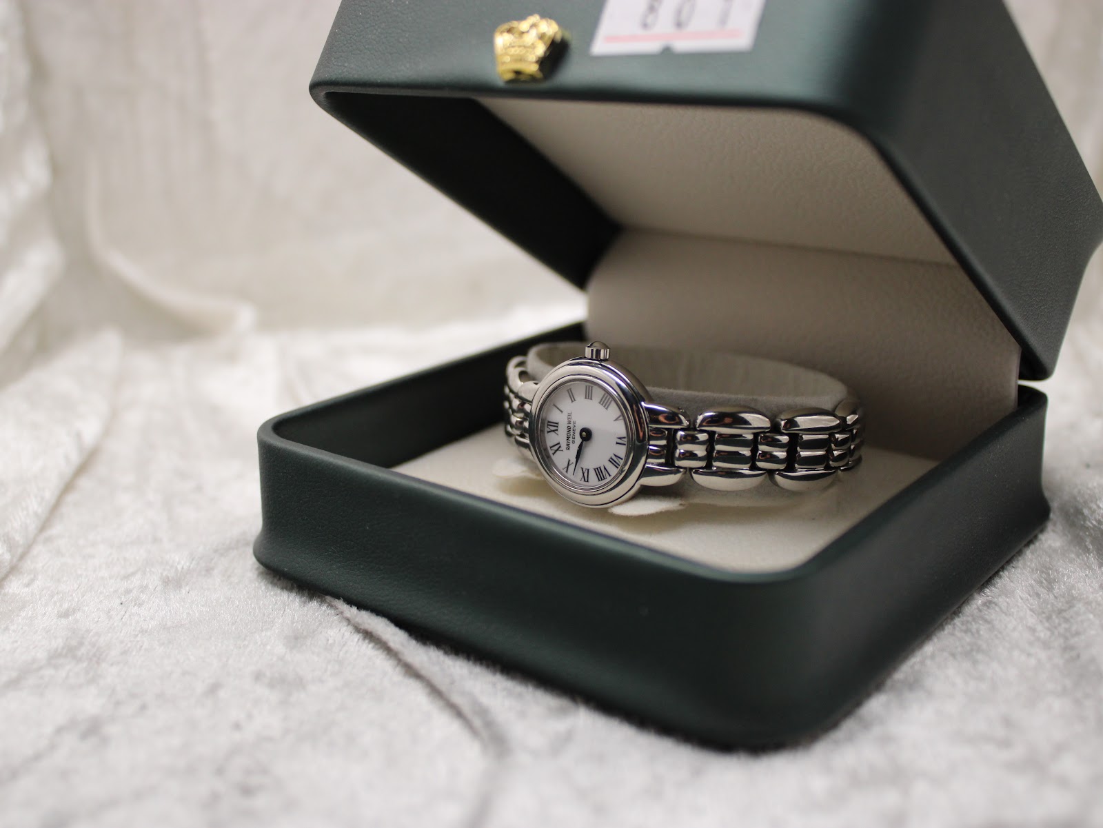 The Raymond Weil Genève 5880 watch displayed inside an open green presentation box, resting on a white cushion.