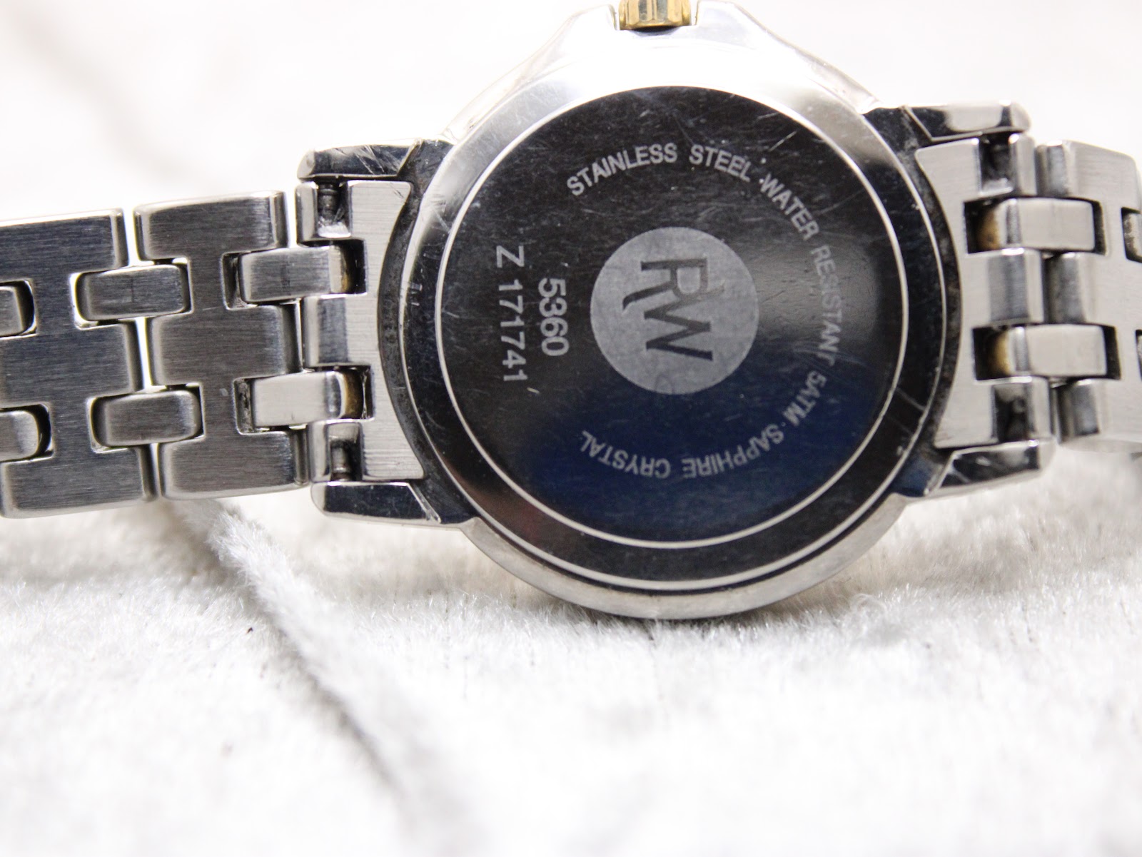 Close-up of the stainless steel case back of the Raymond Weil Tango, showing model 5360, serial Z171741, and 'Stainless Steel Water Resistant 5ATM Sapphire Crystal' engraving.