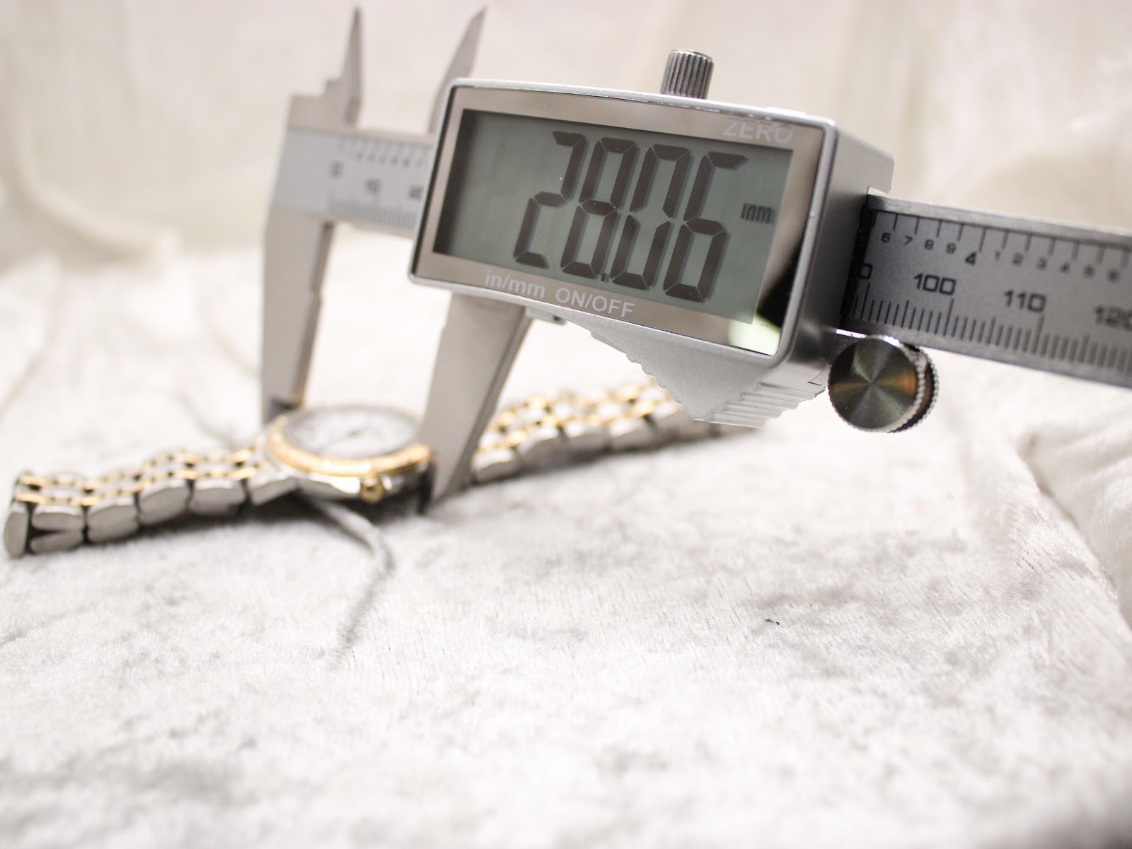 Digital caliper measuring the case diameter of the Raymond Weil Tango watch, with the display showing an exact measurement of 28.06 mm.