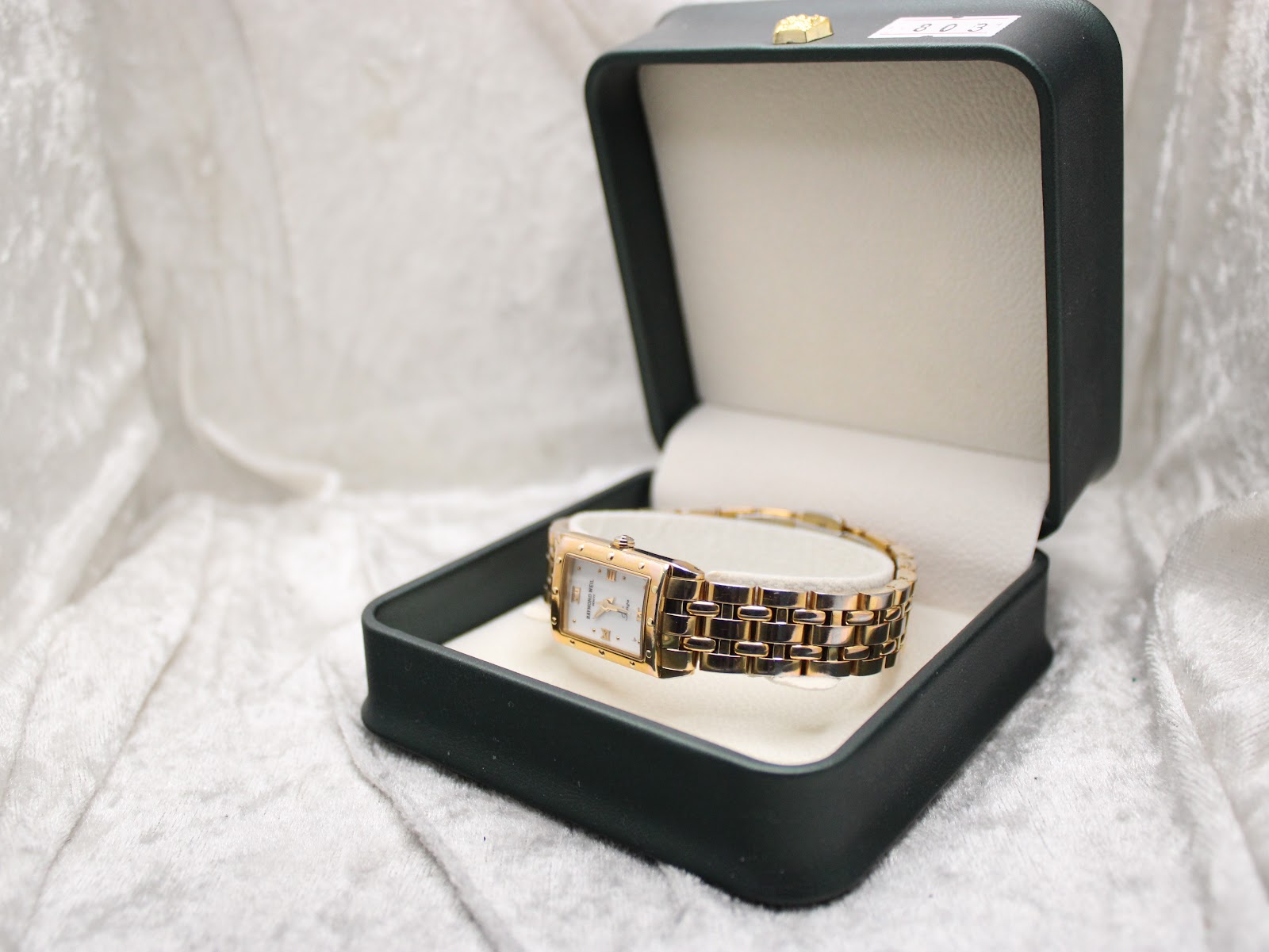 The Raymond Weil Tango watch presented inside a dark green watch box with a soft cream interior lining.