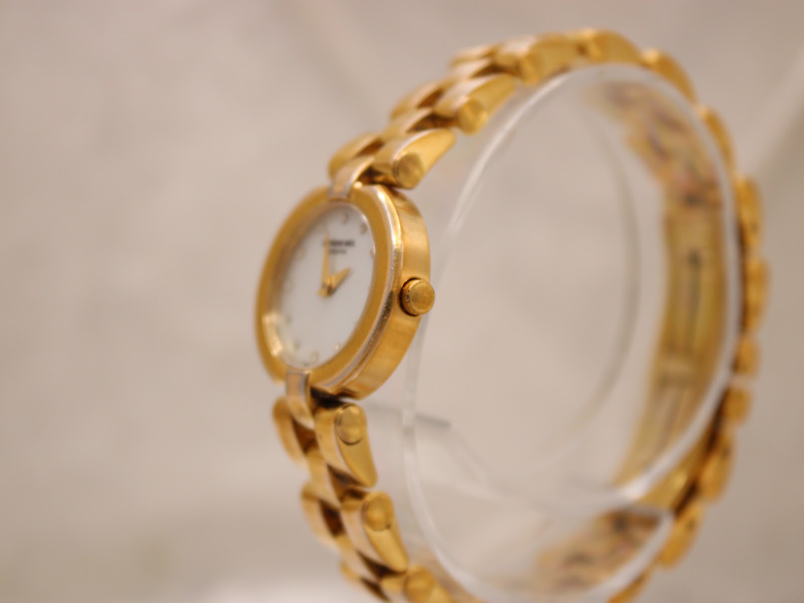 Side view of the Raymond Weil watch on a clear stand, showing the crown and case profile.