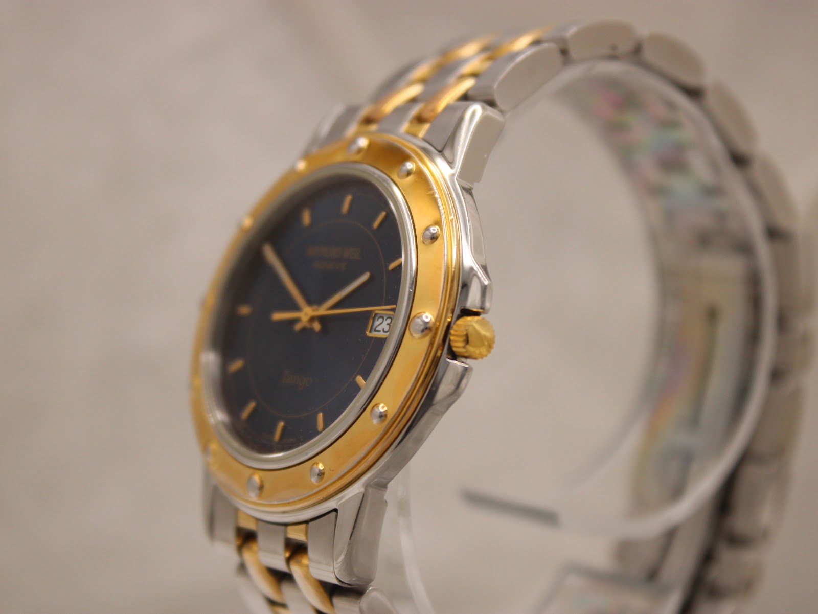 Angled side view of the Raymond Weil Tango watch, highlighting the two-tone case and bracelet on a stand.