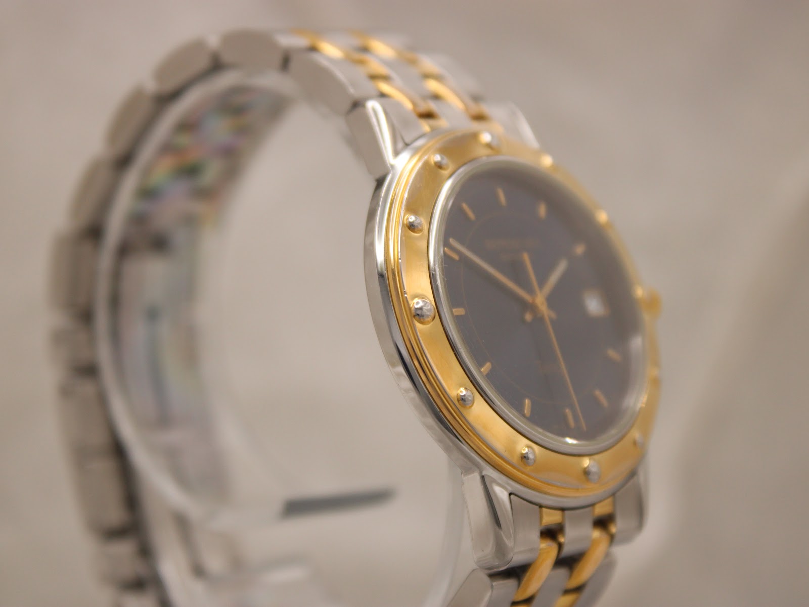 Another angled side view of the Raymond Weil Tango on a clear stand, focusing on the two-tone bezel and crown.