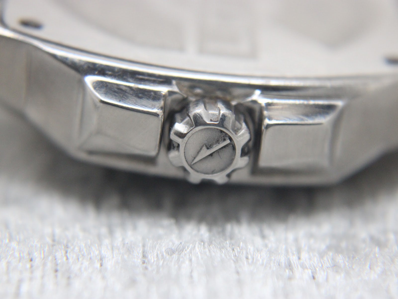 Extreme close-up of the watch crown, clearly showing the engraved Lotus logo on its textured surface.