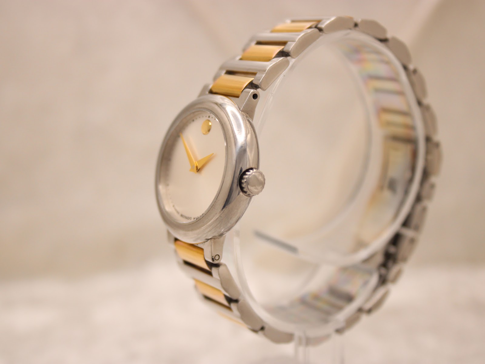 Side view of the Movado Concerto watch on a clear stand, showing the curved case profile and two-tone bracelet links.