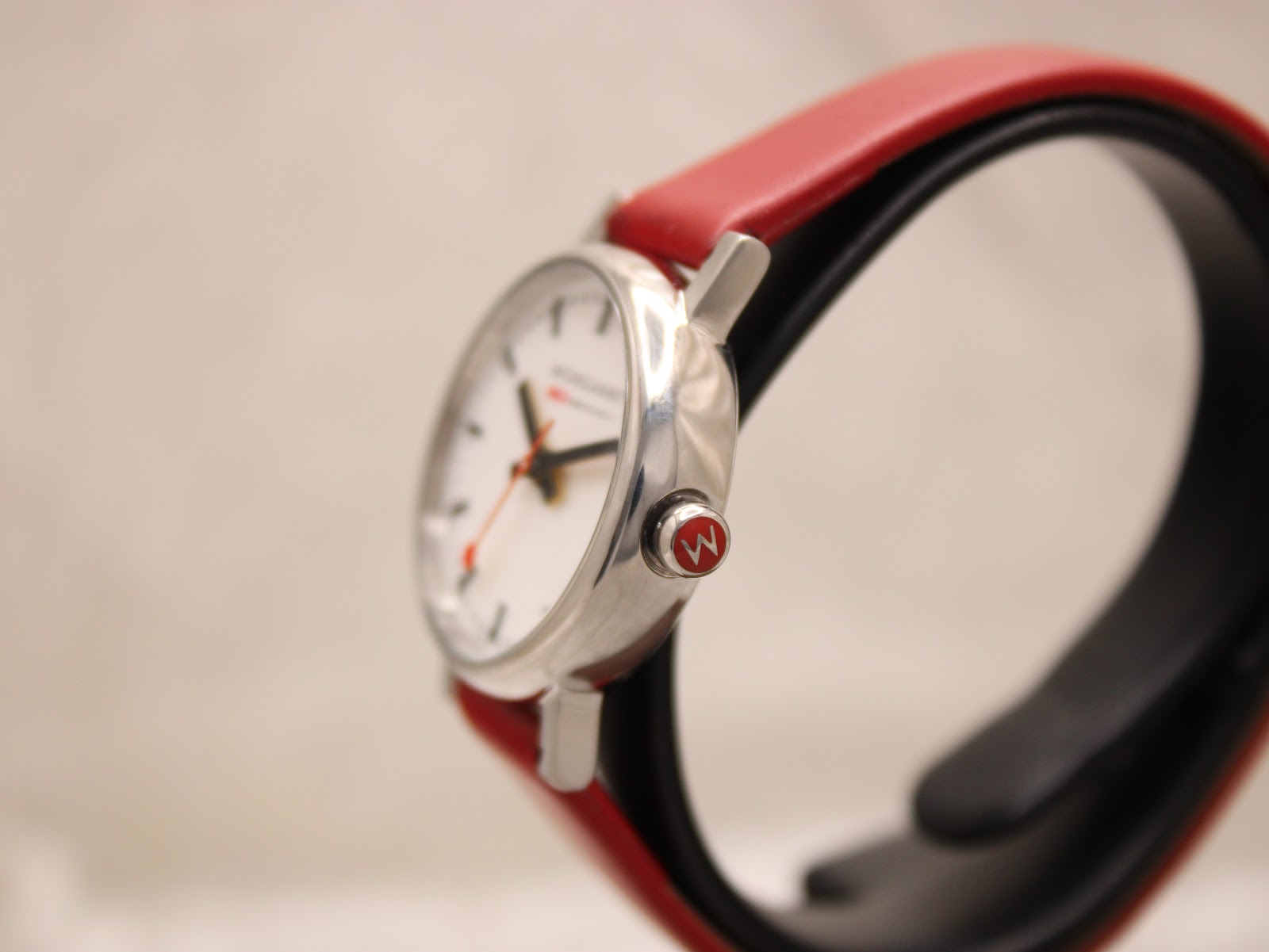 Side profile of the Mondaine watch, highlighting the polished stainless steel case and the distinctive red-crowned winder.