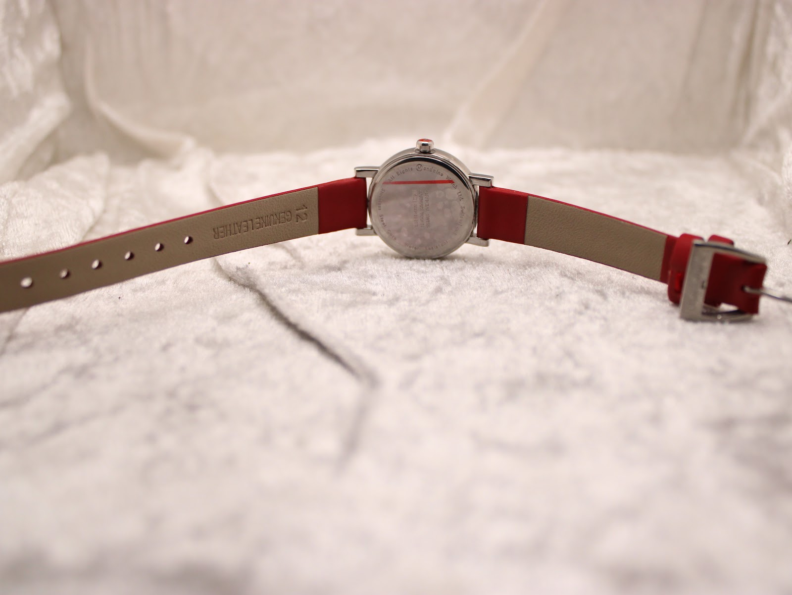 Full back view of the Mondaine watch with the red leather strap fully extended, clearly showing the case back and "GENUINE LEATHER" embossed on the strap.