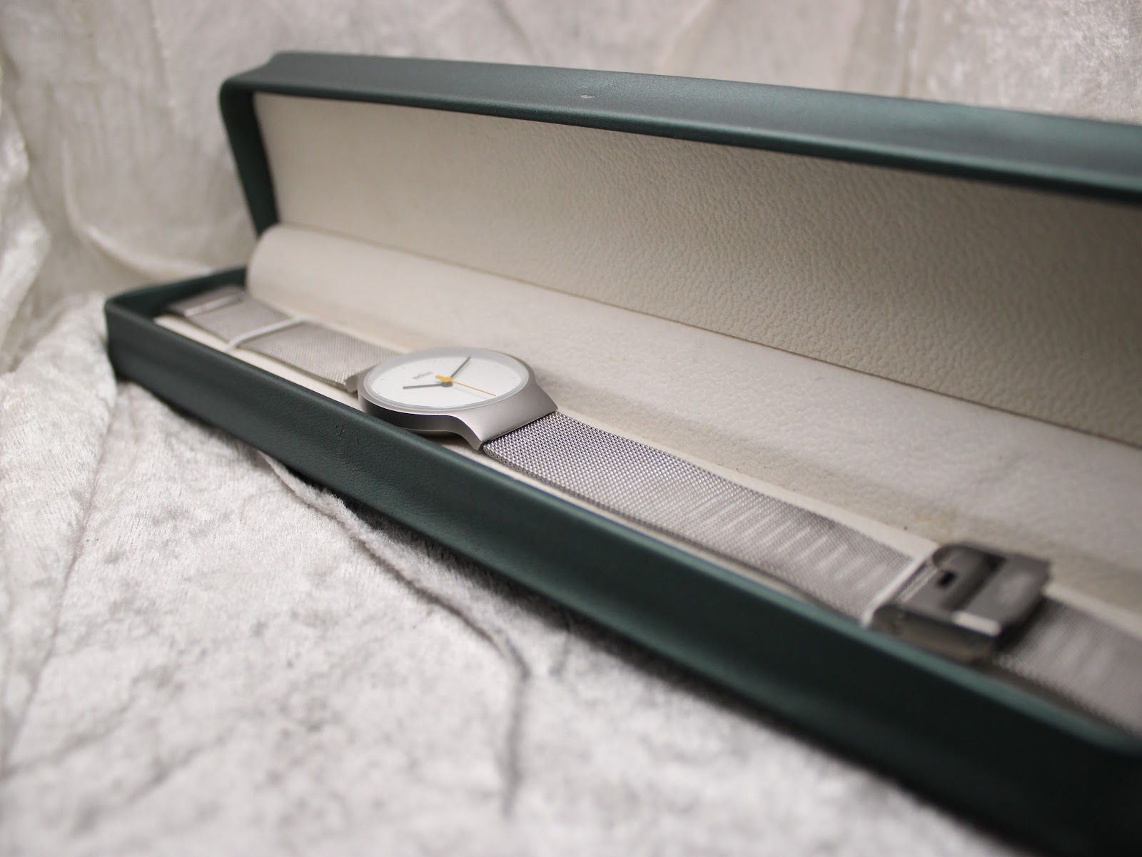 The Braun BN0211 watch with its silver mesh bracelet laid inside a dark green presentation box with a cream-coloured interior.