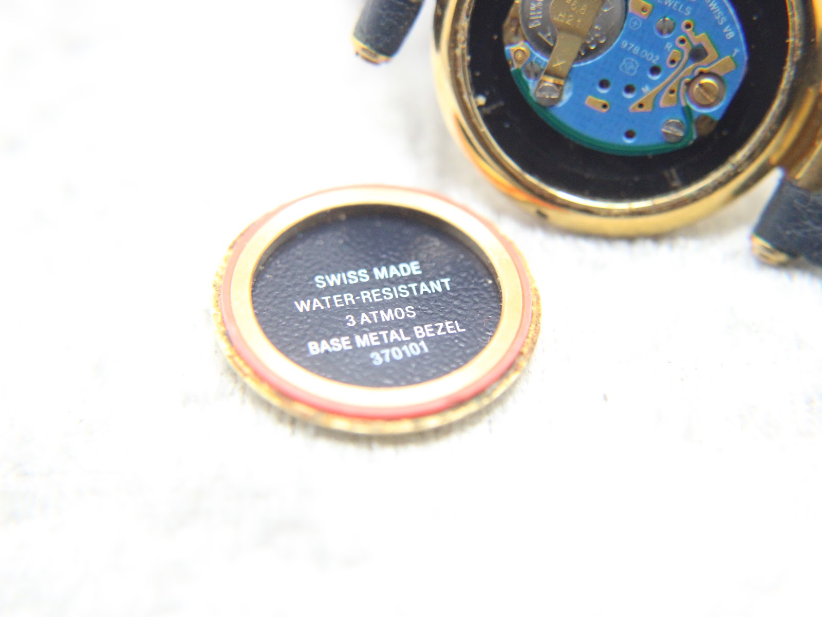 Internal view of the case back insert, showing "Swiss Made", "Water-Resistant", "3 ATMOS", "Base Metal Bezel".