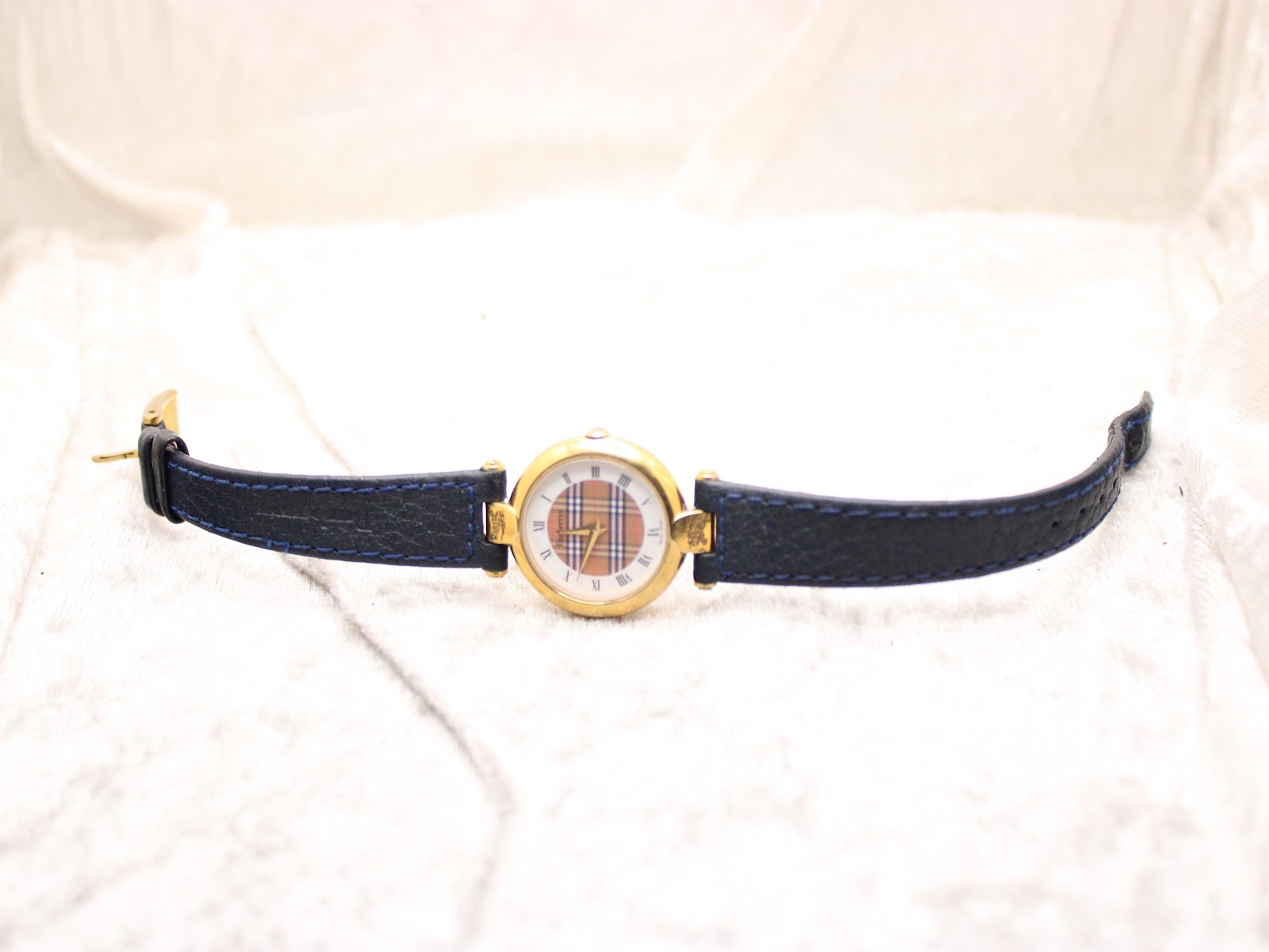 Full view of the Burberrys watch with its blue leather strap unclasped, laid flat on a white surface.