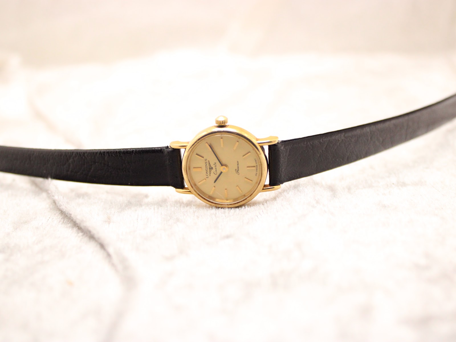 Top-down view of the Longines Présence watch lying flat, displaying the black leather strap and gold-tone case.