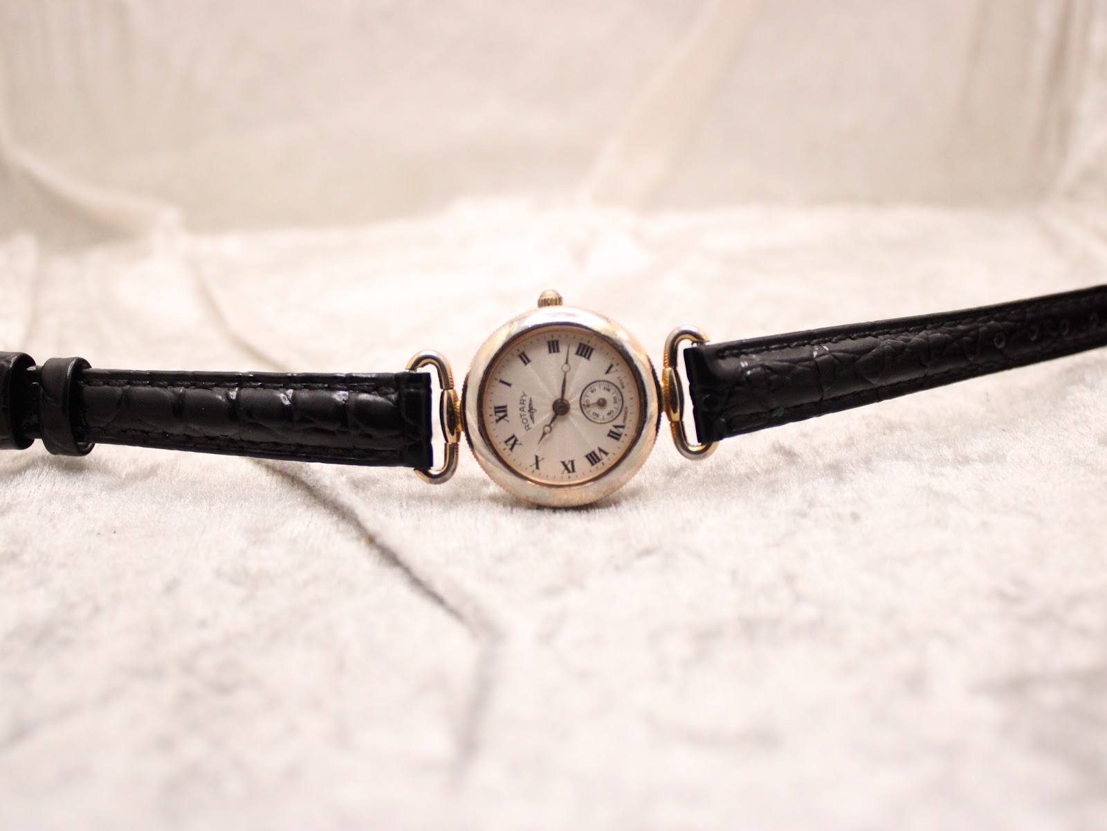 Frontal view of the Rotary watch lying flat on a textured white surface, with its black leather strap extended symmetrically.