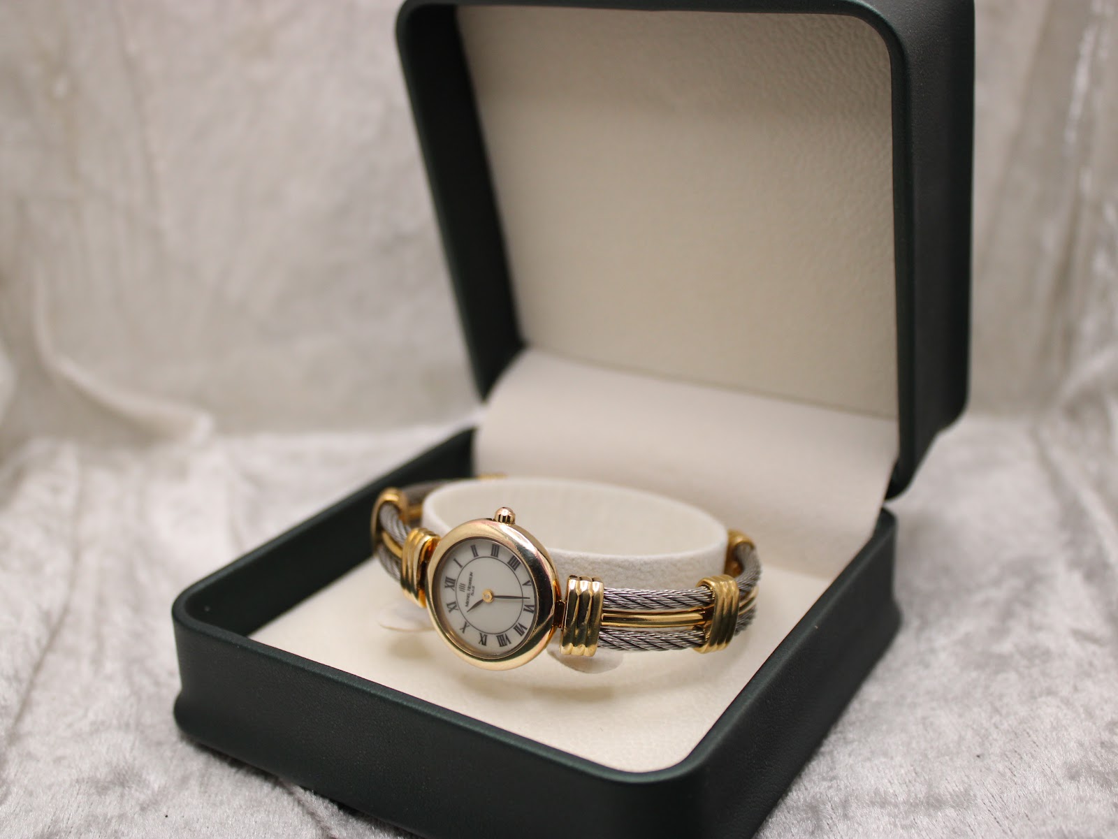 Michel Herbelin watch presented inside an open dark green presentation box on a white textured surface.