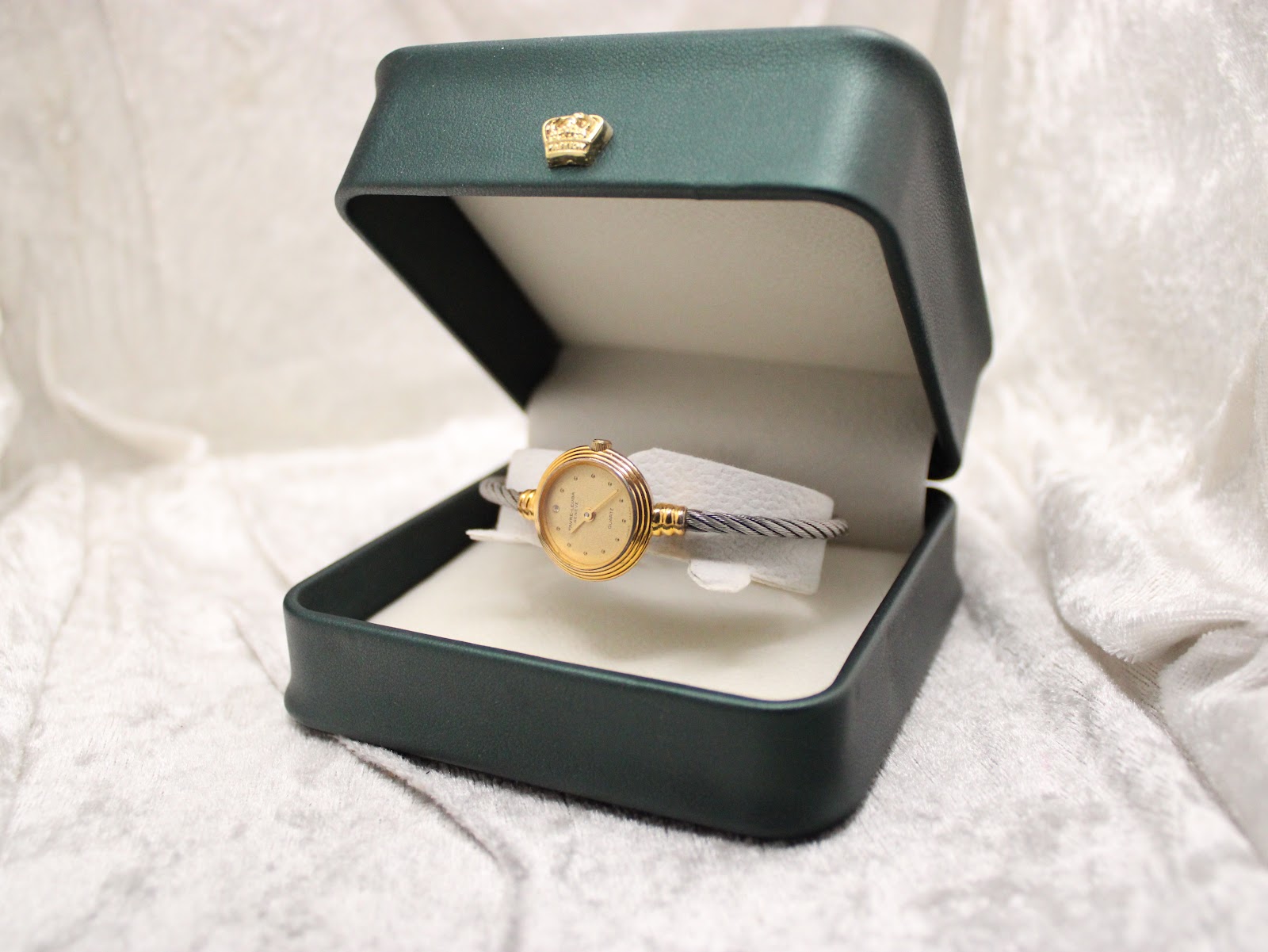 The watch presented in an open dark green watch box with a gold crown emblem on the lid.