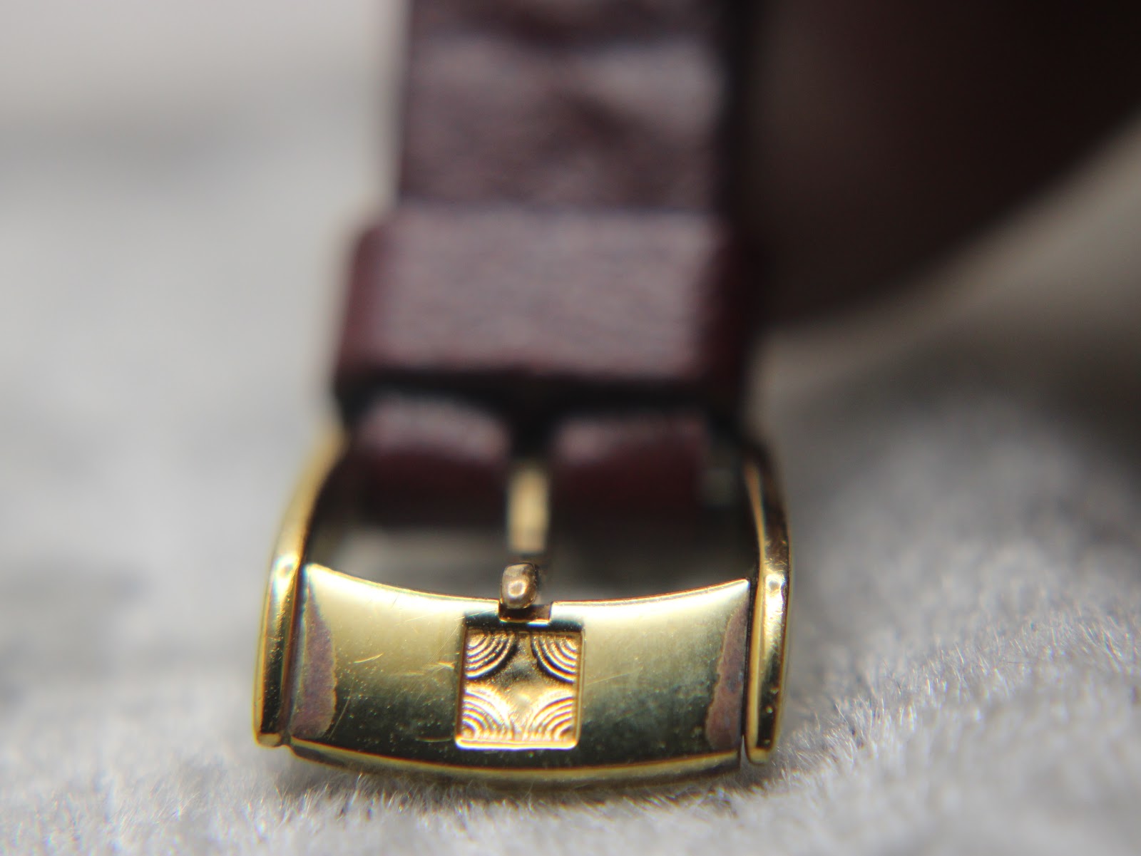 Close-up of the gold-tone Zenith signed buckle on the burgundy leather strap.