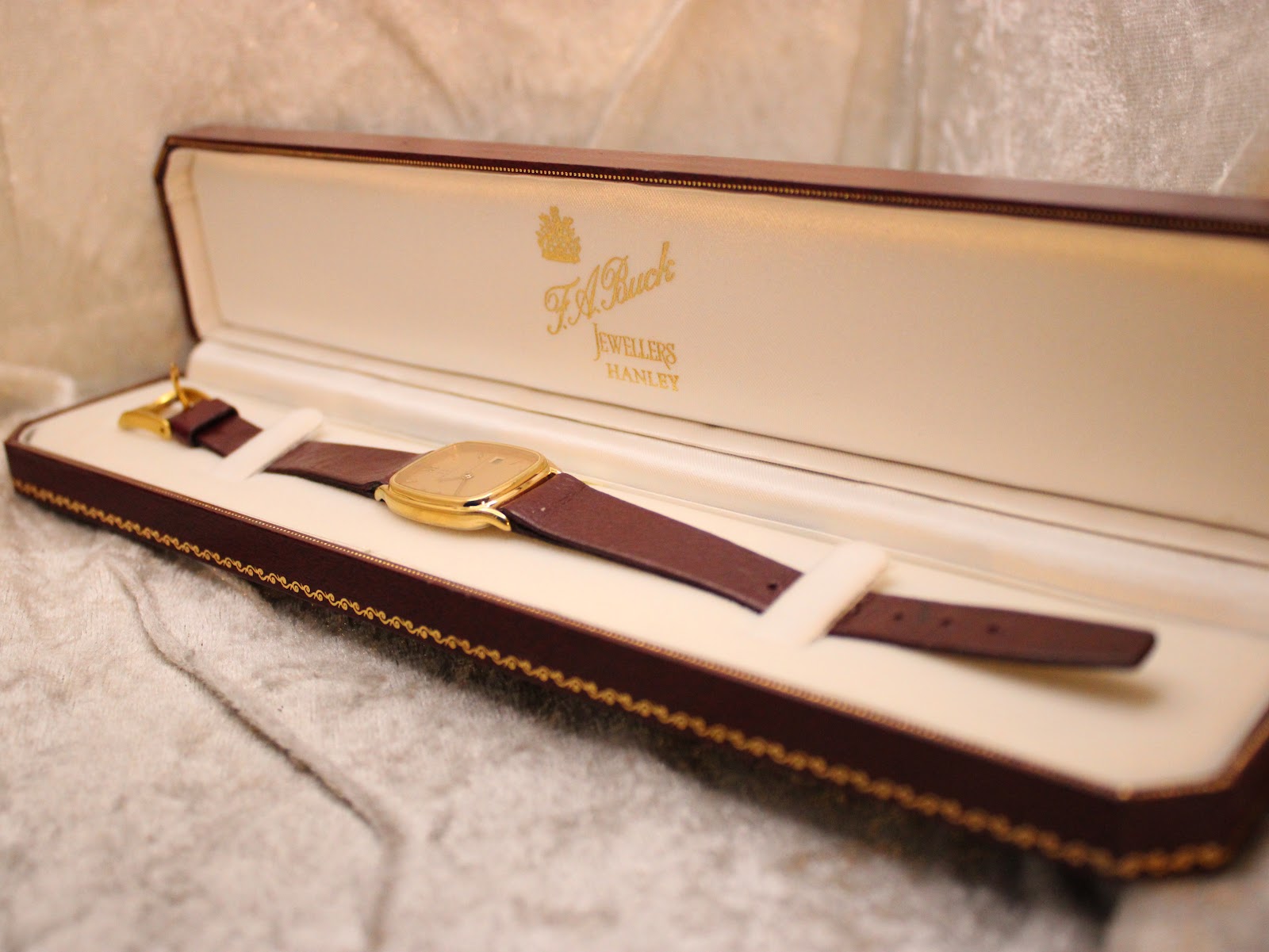 Zenith watch with burgundy strap placed inside a brown display box by F.H. Buck Jewellers.
