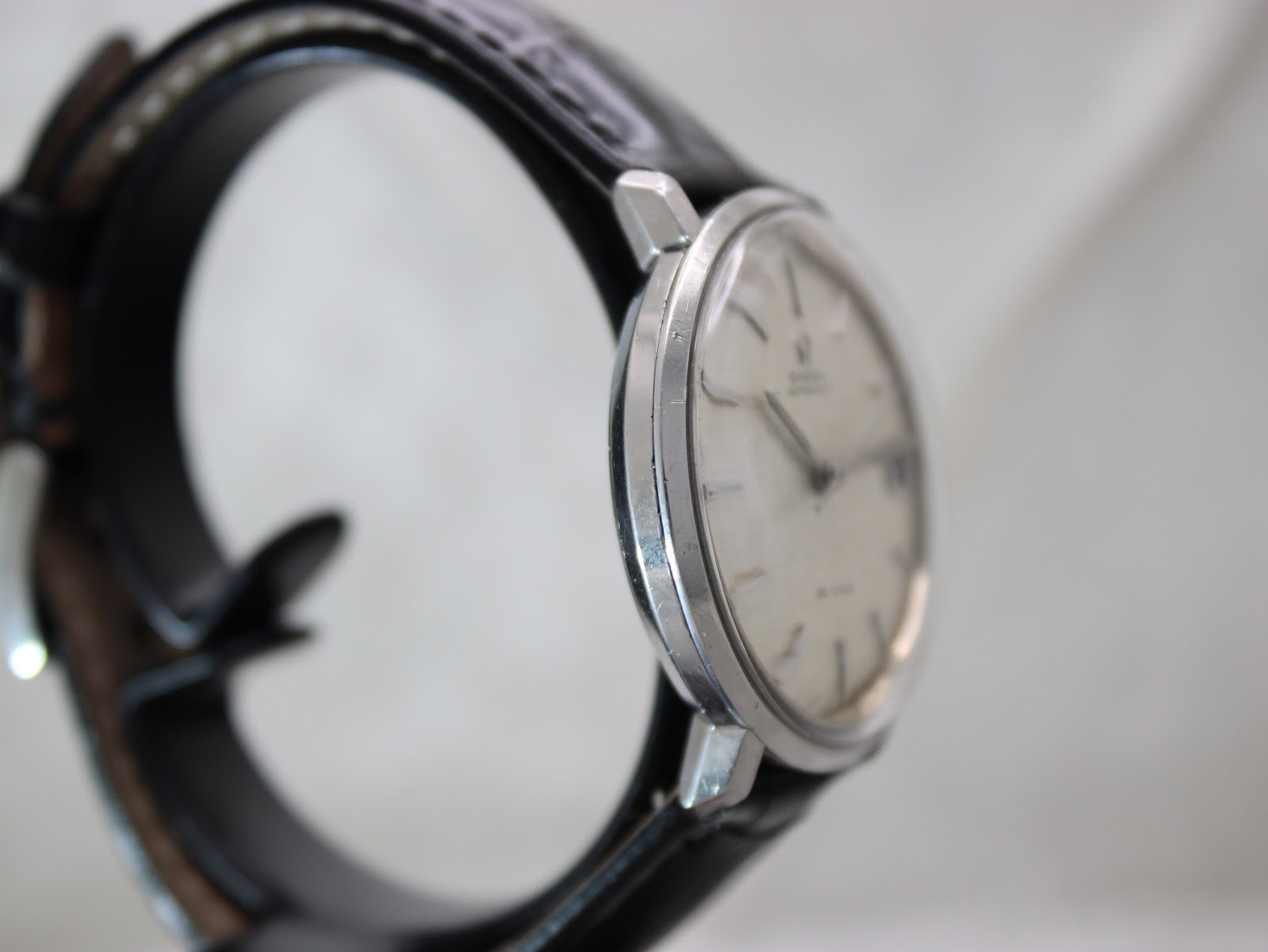 Another angled side view of the Omega De Ville watch, showing the case profile with some wear and reflections on the polished bezel.