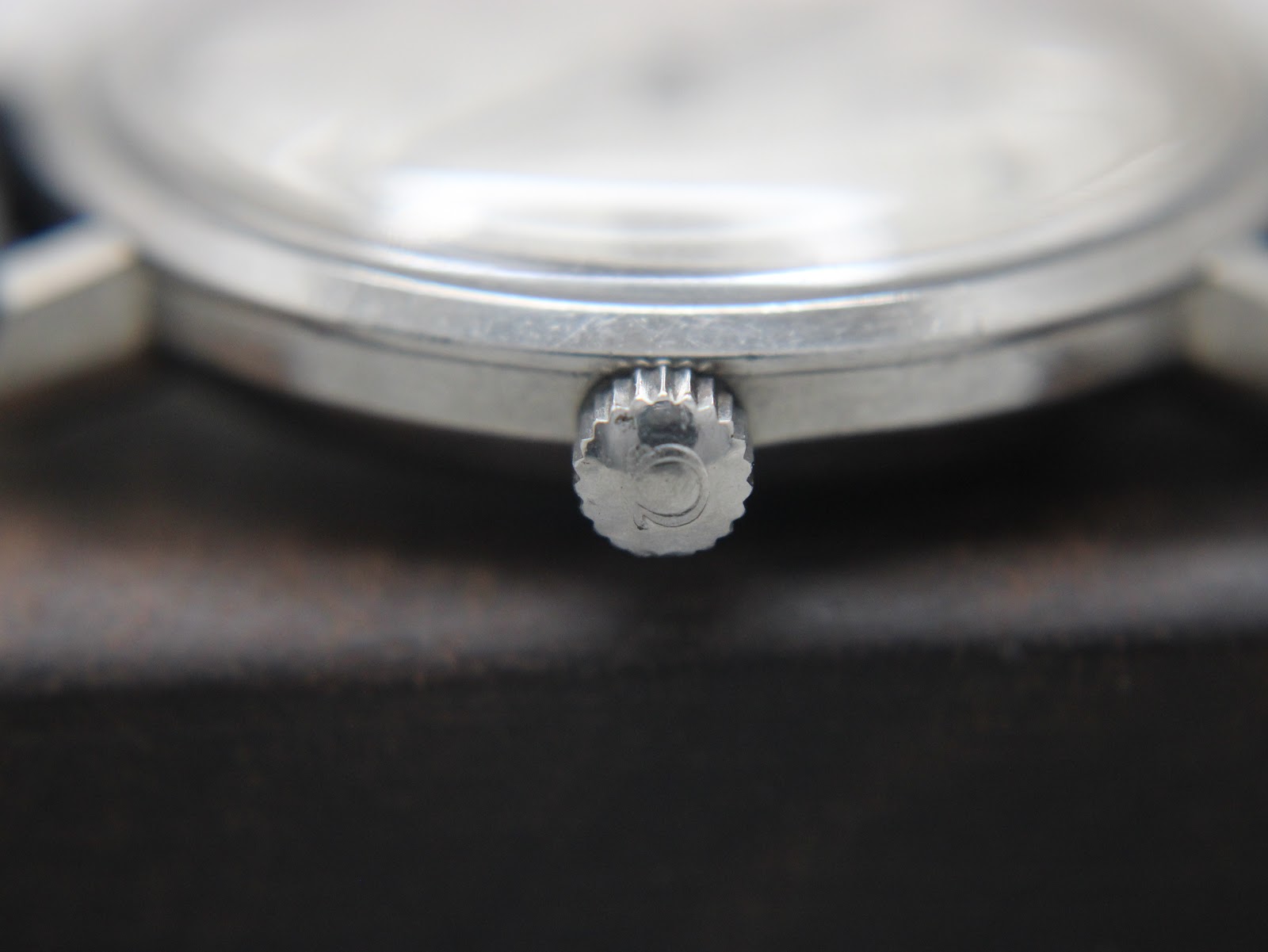 Detailed macro shot of the watch crown, showing the Omega logo (Ω) and the fluted texture.