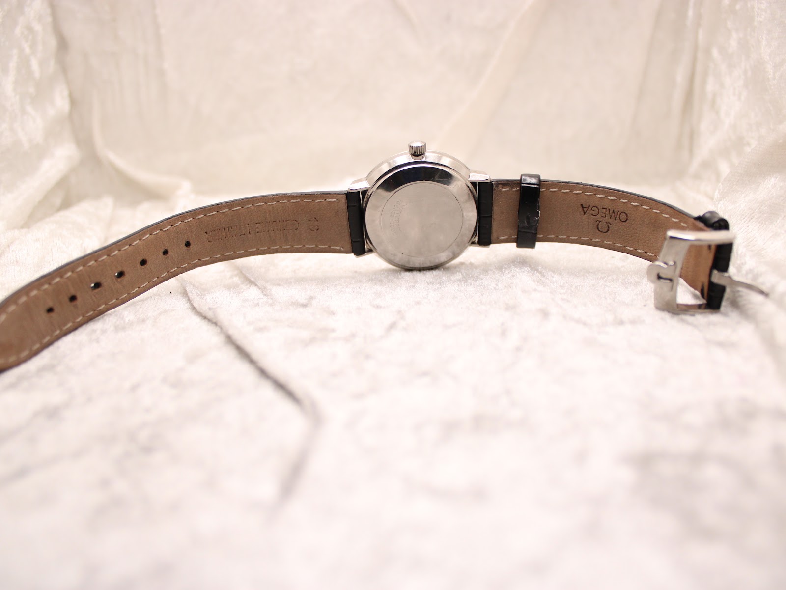 Overhead view of the Omega De Ville watch from the rear, displaying the full length of the black leather strap with its brown underside and a plain buckle.