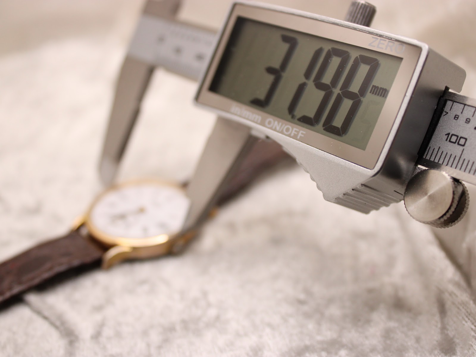 A digital caliper measuring the watch case, with the display showing a precise diameter of 31.98mm.