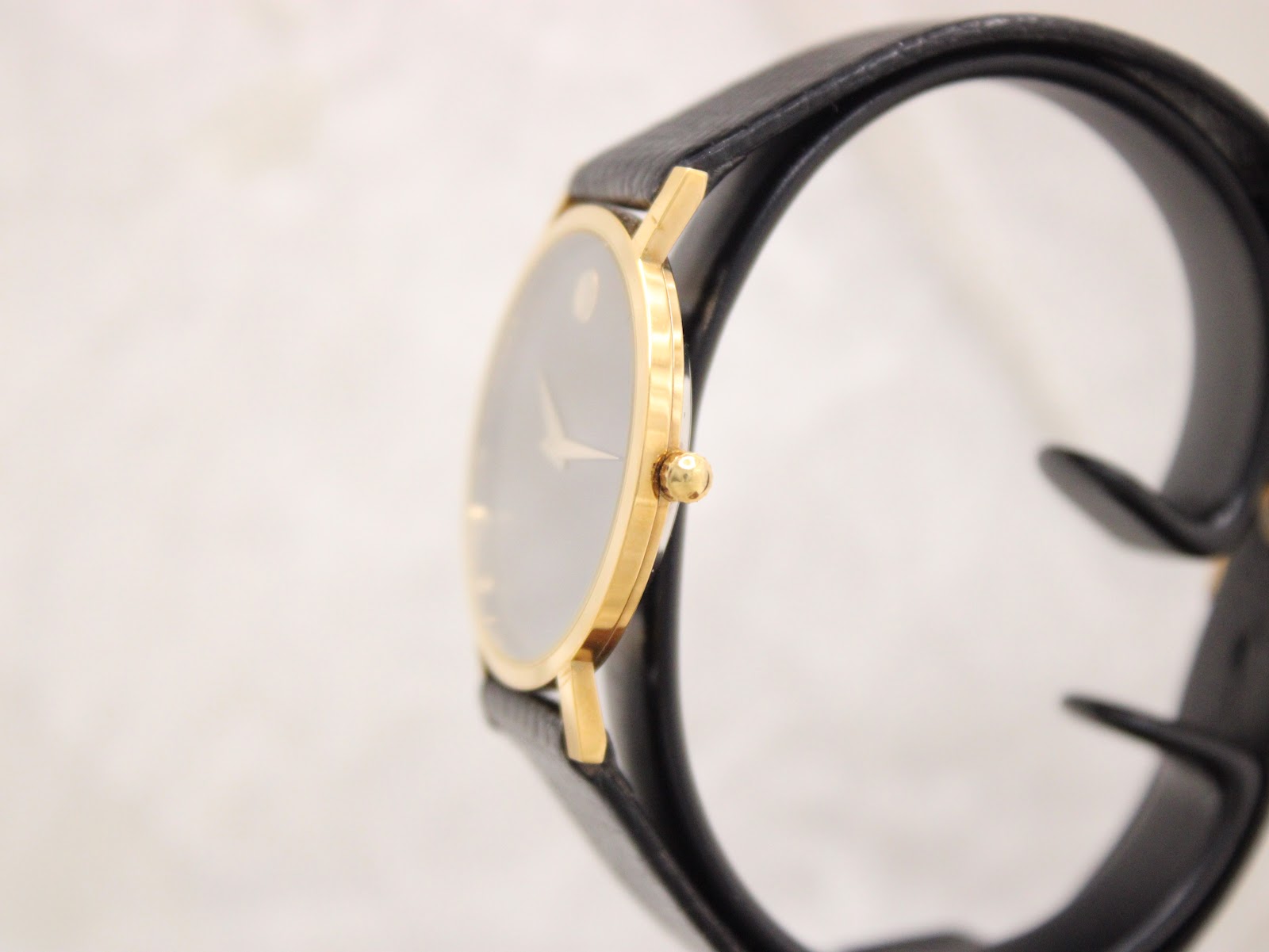Side profile of the Movado Museum watch, highlighting its thin gold-plated case and crown on a watch stand.